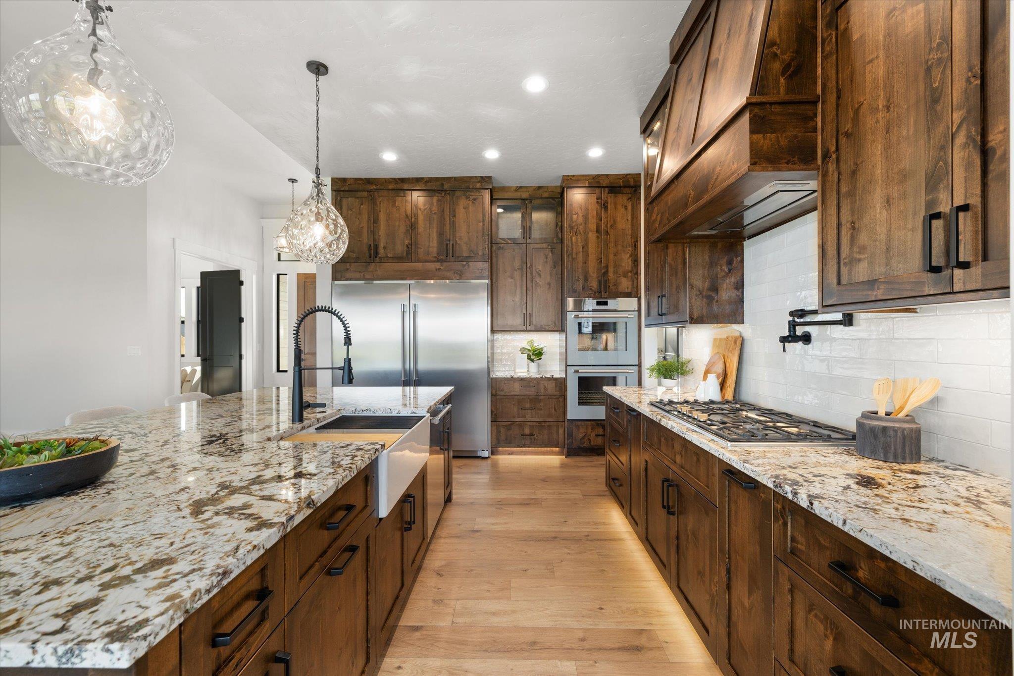 Kitchen featuring light wood-style flooring, light stone countertops, decorative light fixtures, recessed lighting, and appliances with stainless steel finishes