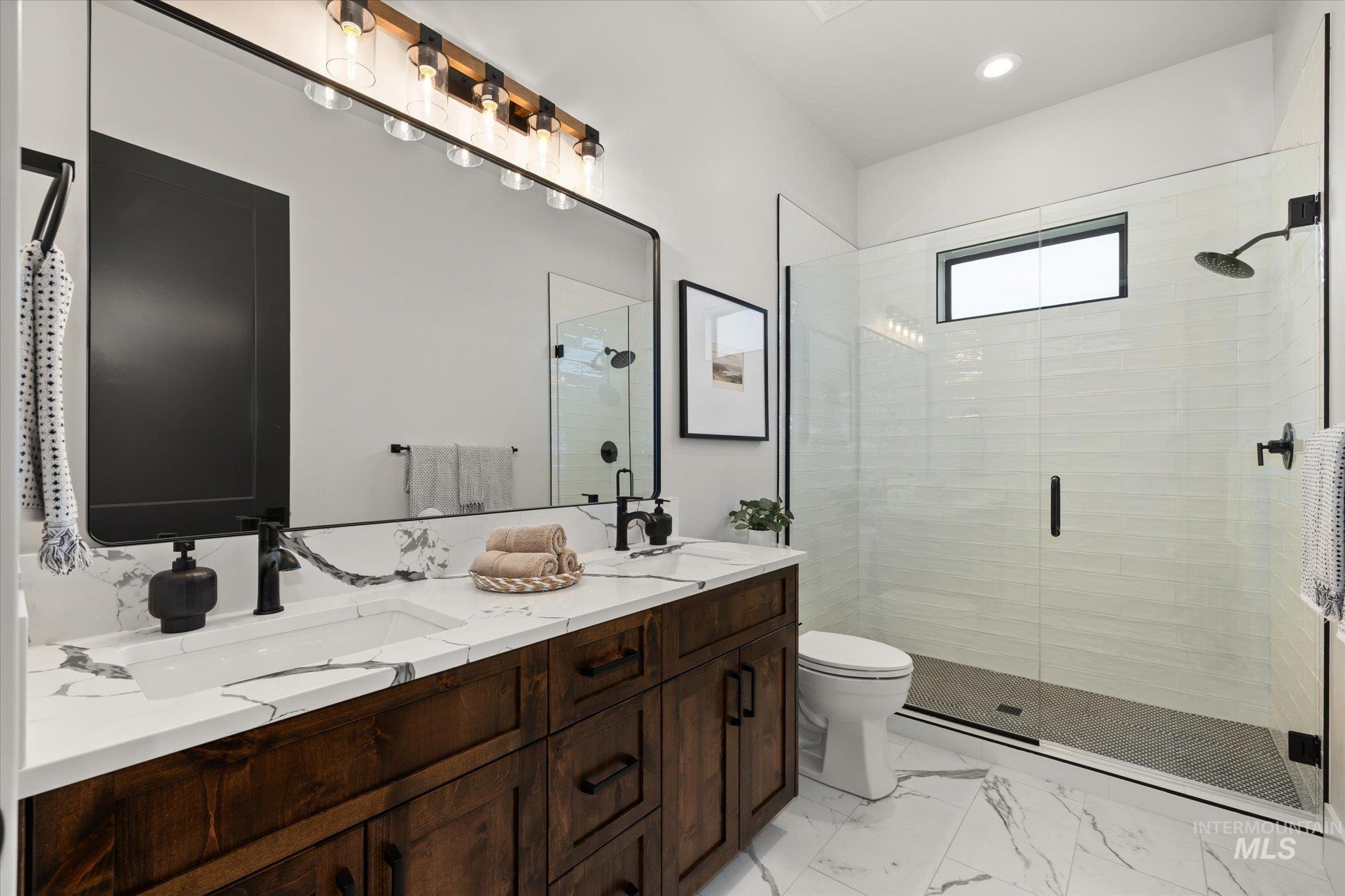 Full bathroom featuring a stall shower, double vanity, light marble finish floors, and recessed lighting