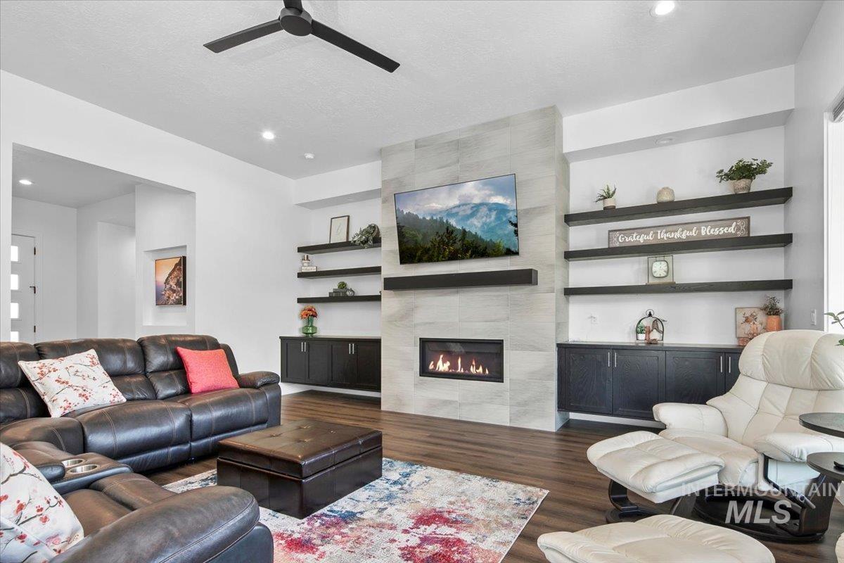 Living room featuring wood finished floors, a fireplace, recessed lighting, built in shelves, and a ceiling fan