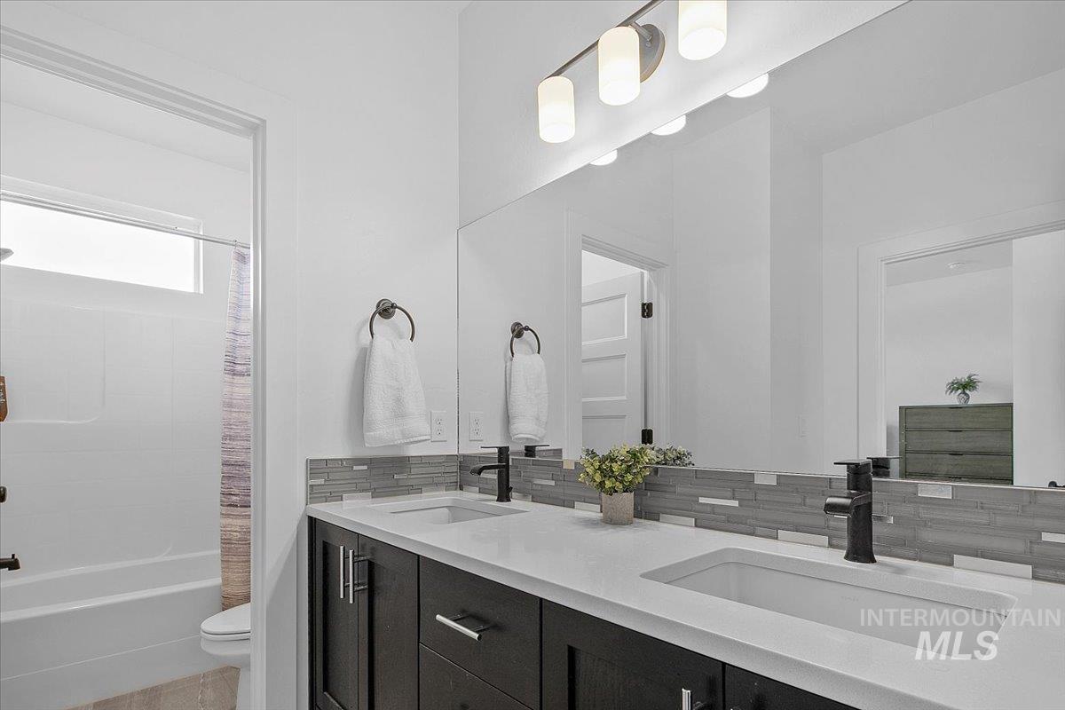 Bathroom with tasteful backsplash, shower / bath combo with shower curtain, and double vanity