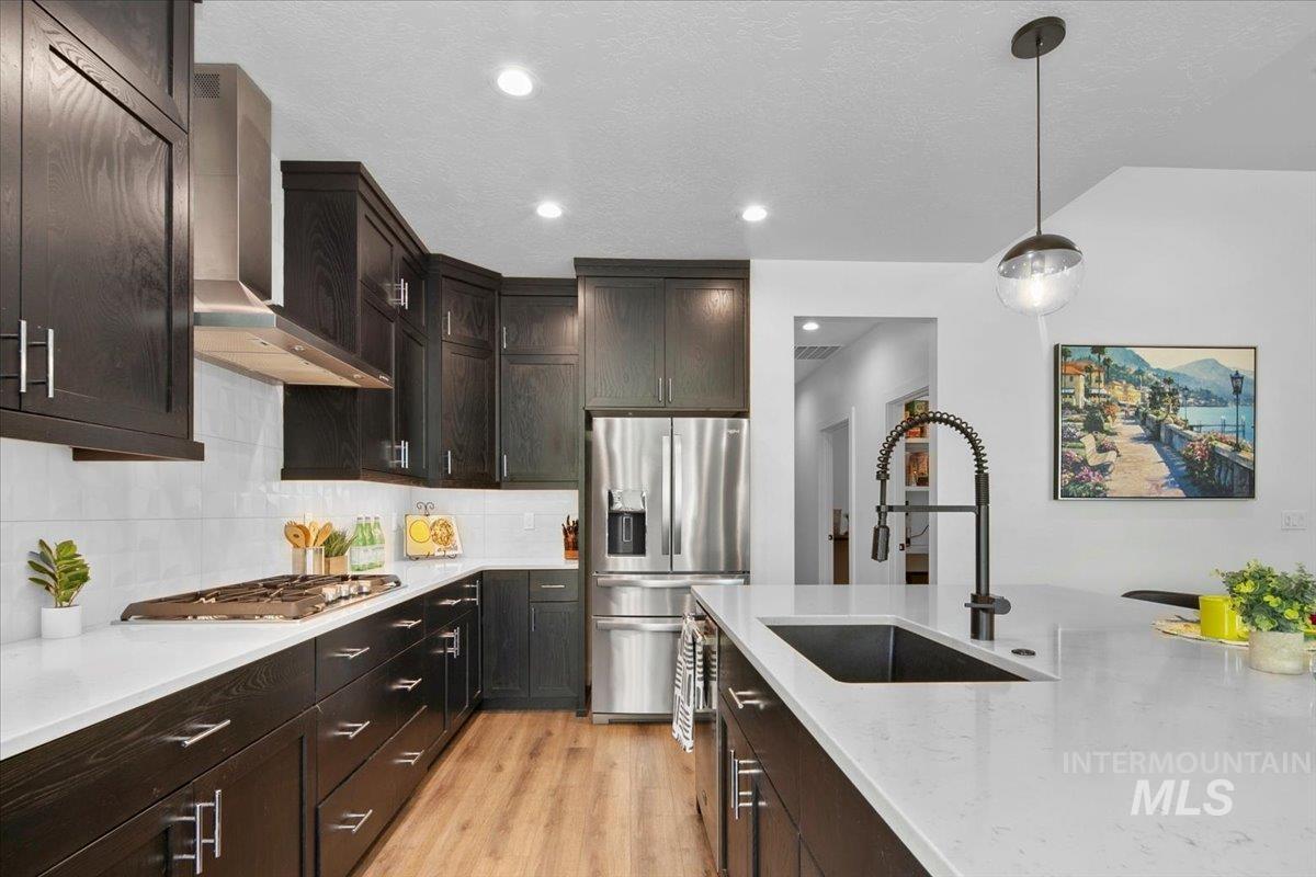 Kitchen featuring pendant lighting, light wood-style floors, decorative backsplash, appliances with stainless steel finishes, and dark brown cabinets