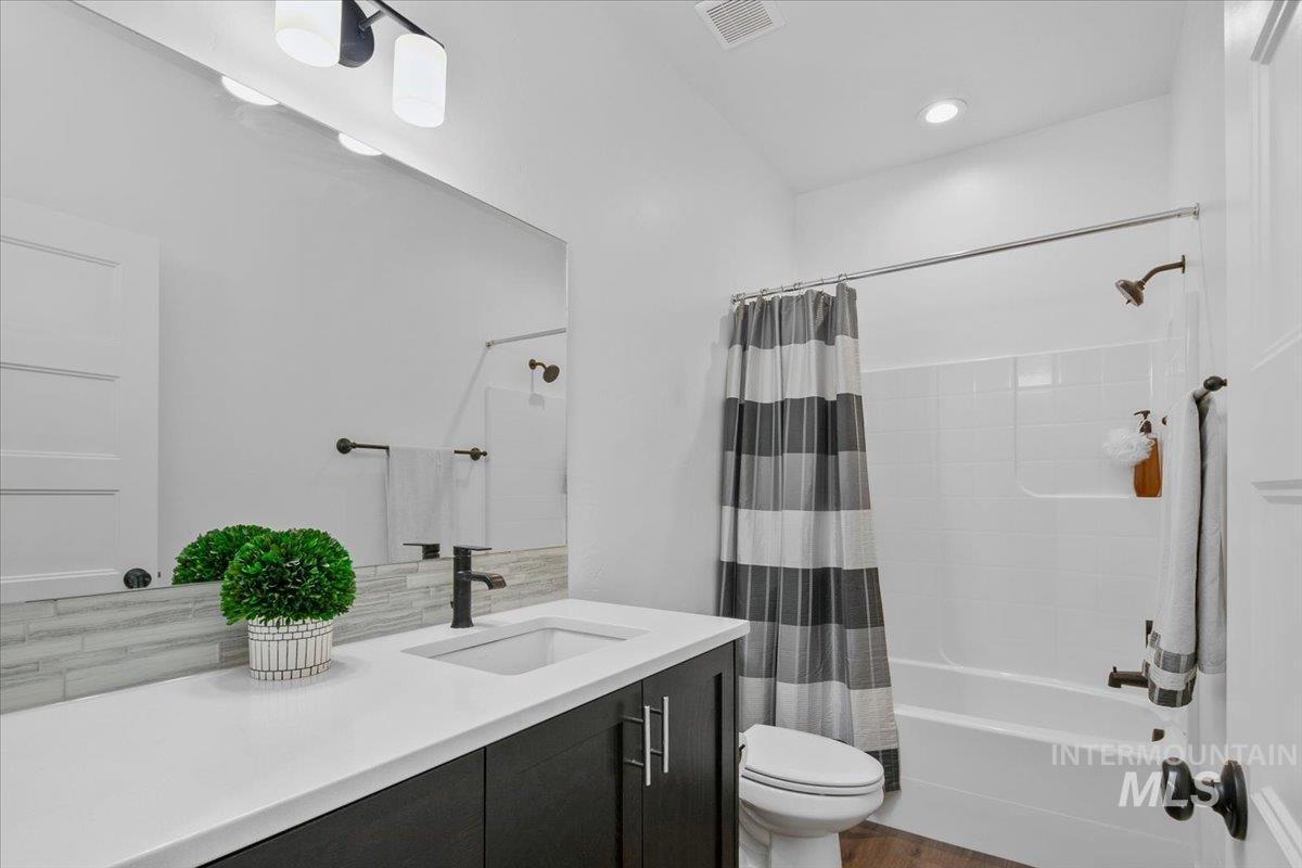 Full bathroom featuring shower / tub combo with curtain, vanity, and dark wood-style flooring