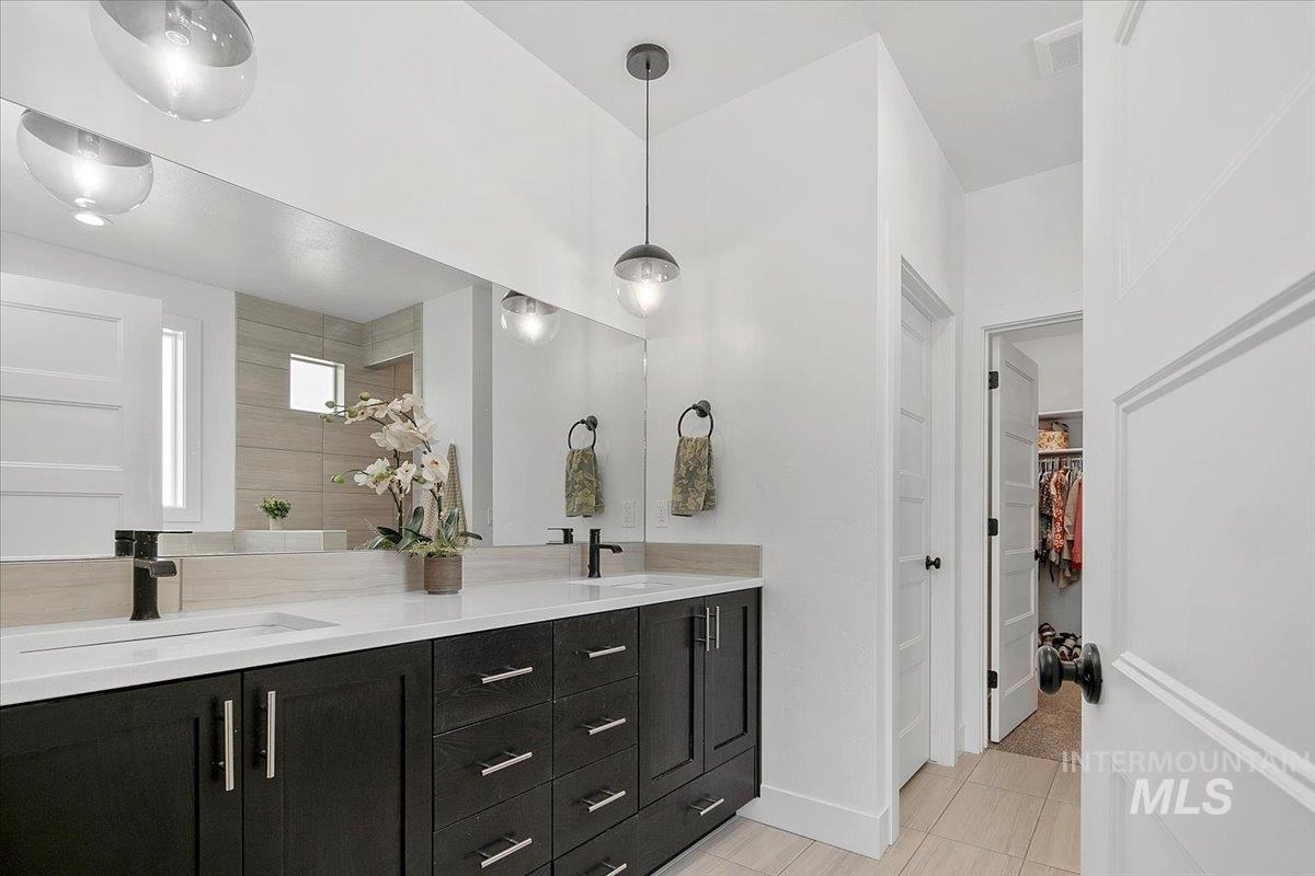 Bathroom with a walk in closet, double vanity, and light tile patterned floors