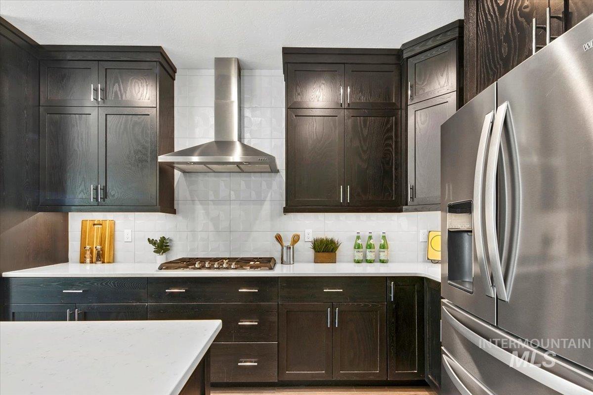 Kitchen with appliances with stainless steel finishes, wall chimney range hood, tasteful backsplash, and light stone countertops