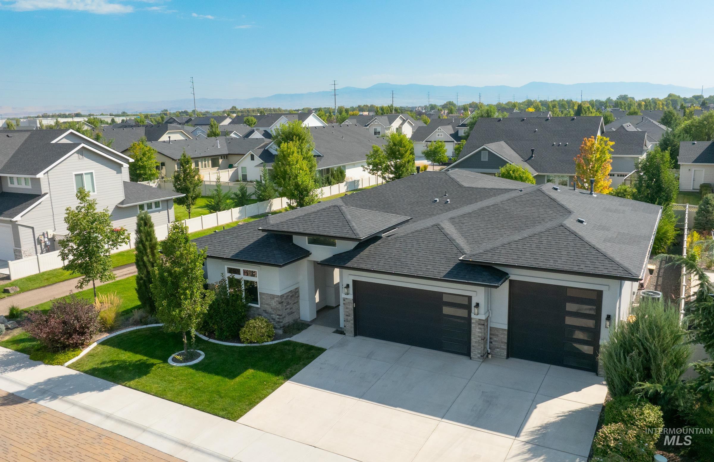 View of front of home featuring an attached garage, stone siding, concrete driveway, roof with shingles, and a front yard