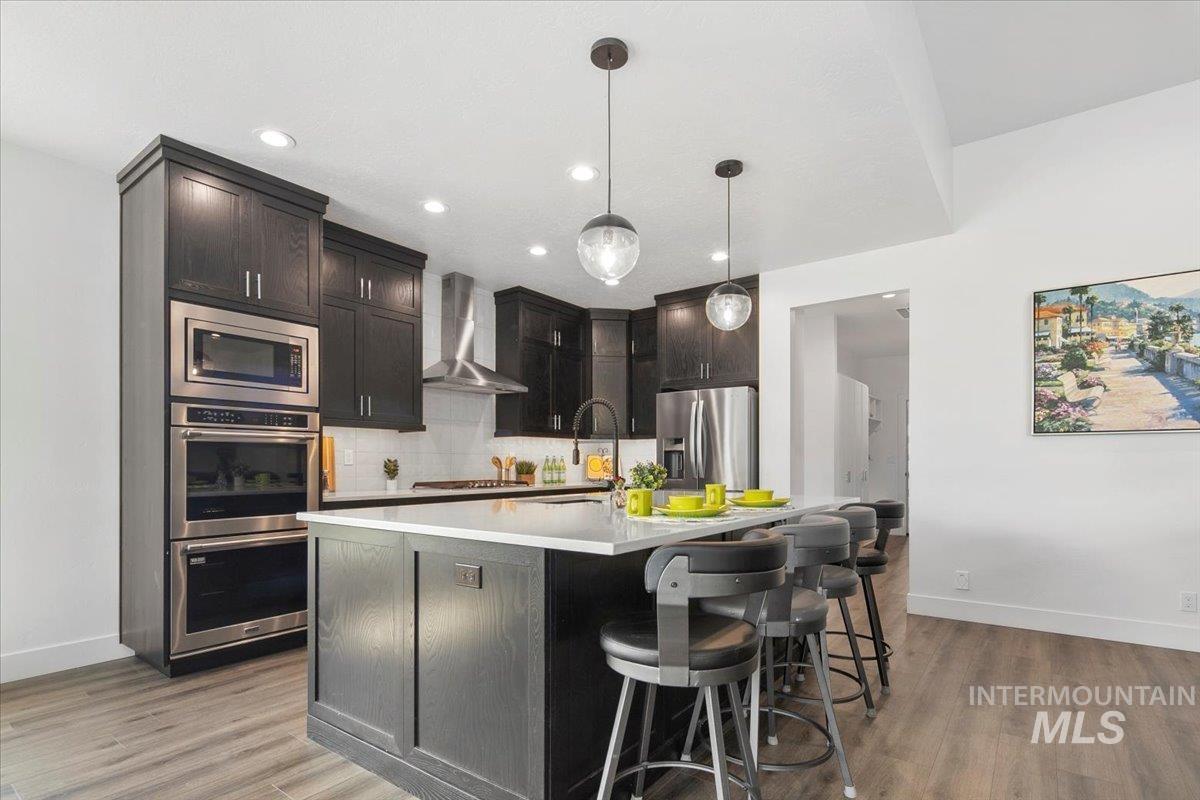 Kitchen featuring decorative light fixtures, decorative backsplash, stainless steel appliances, wall chimney range hood, and a kitchen bar