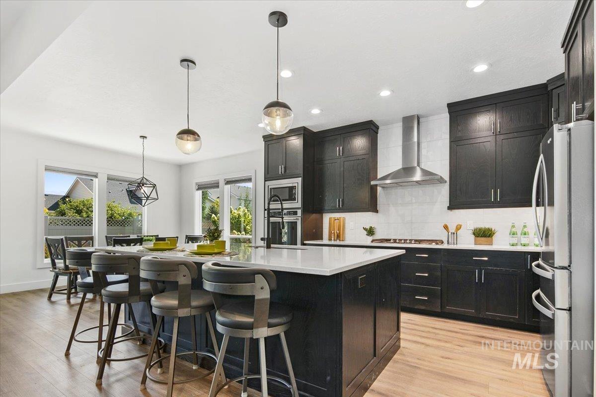 Kitchen featuring dark cabinetry, backsplash, decorative light fixtures, appliances with stainless steel finishes, and a breakfast bar