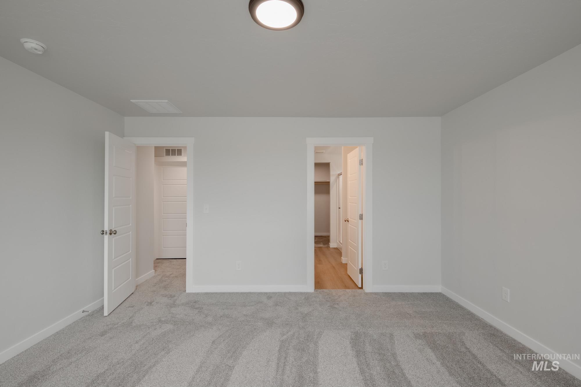 Unfurnished bedroom with light carpet, a walk in closet, and ensuite bath