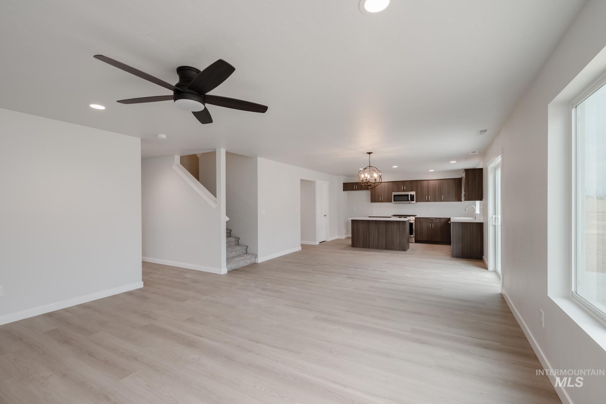 Unfurnished living room featuring recessed lighting, a chandelier, light wood finished floors, a ceiling fan, and stairs
