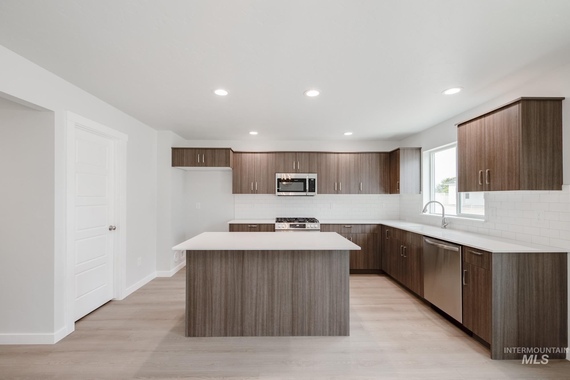 Kitchen featuring tasteful backsplash, modern cabinets, light wood finished floors, appliances with stainless steel finishes, and a center island