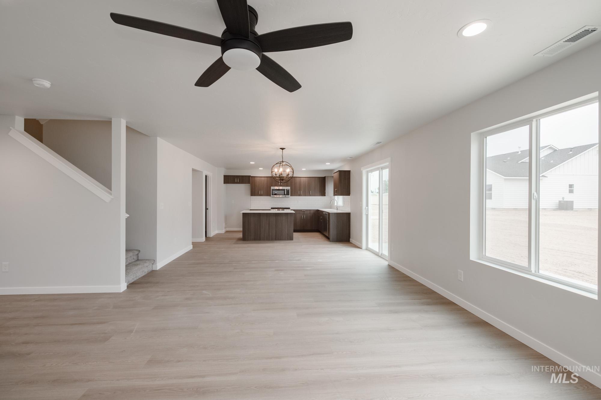 Unfurnished living room featuring light wood-type flooring, recessed lighting, a chandelier, a ceiling fan, and stairs