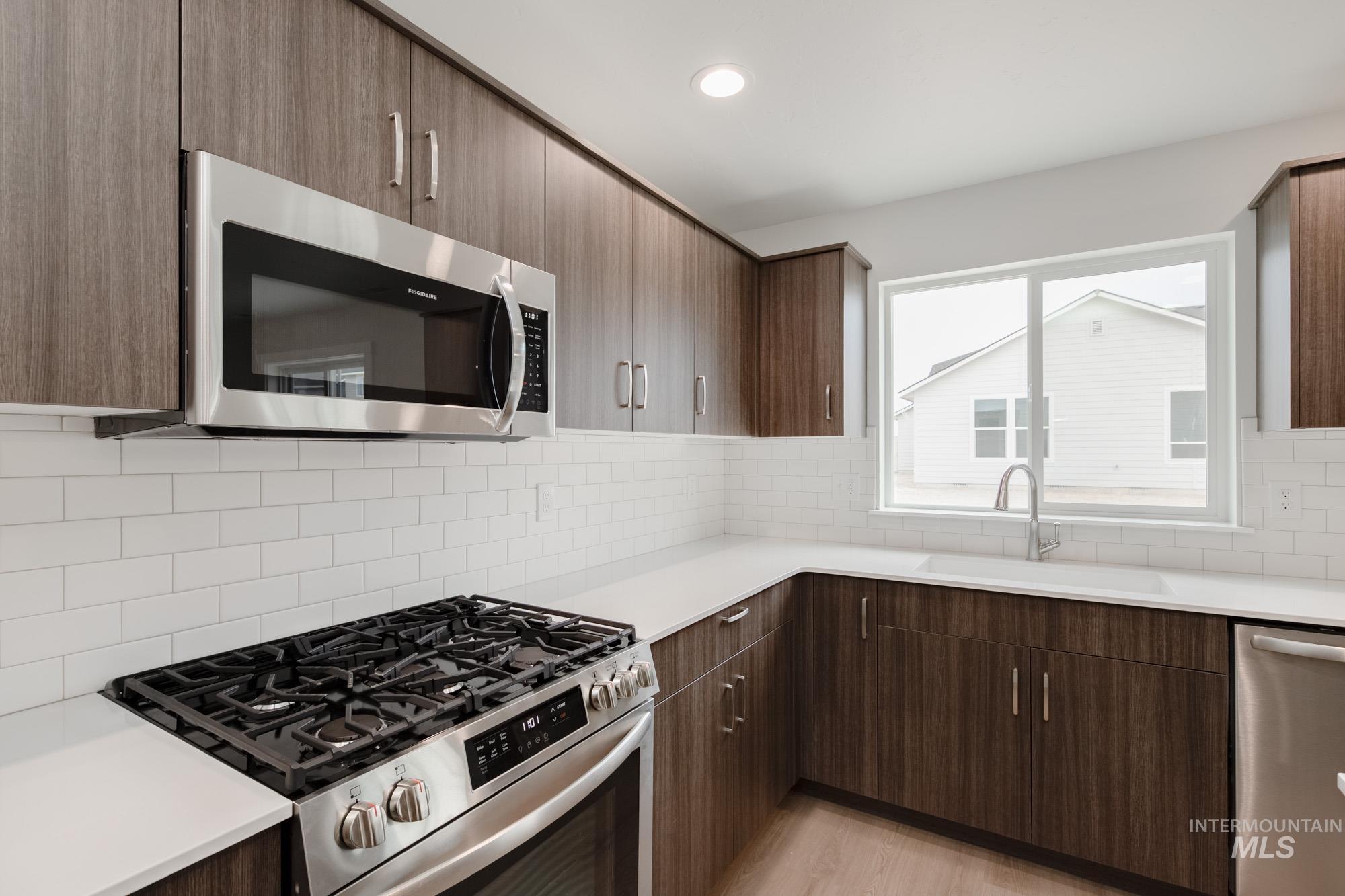 Kitchen with appliances with stainless steel finishes, backsplash, recessed lighting, dark brown cabinets, and light stone countertops