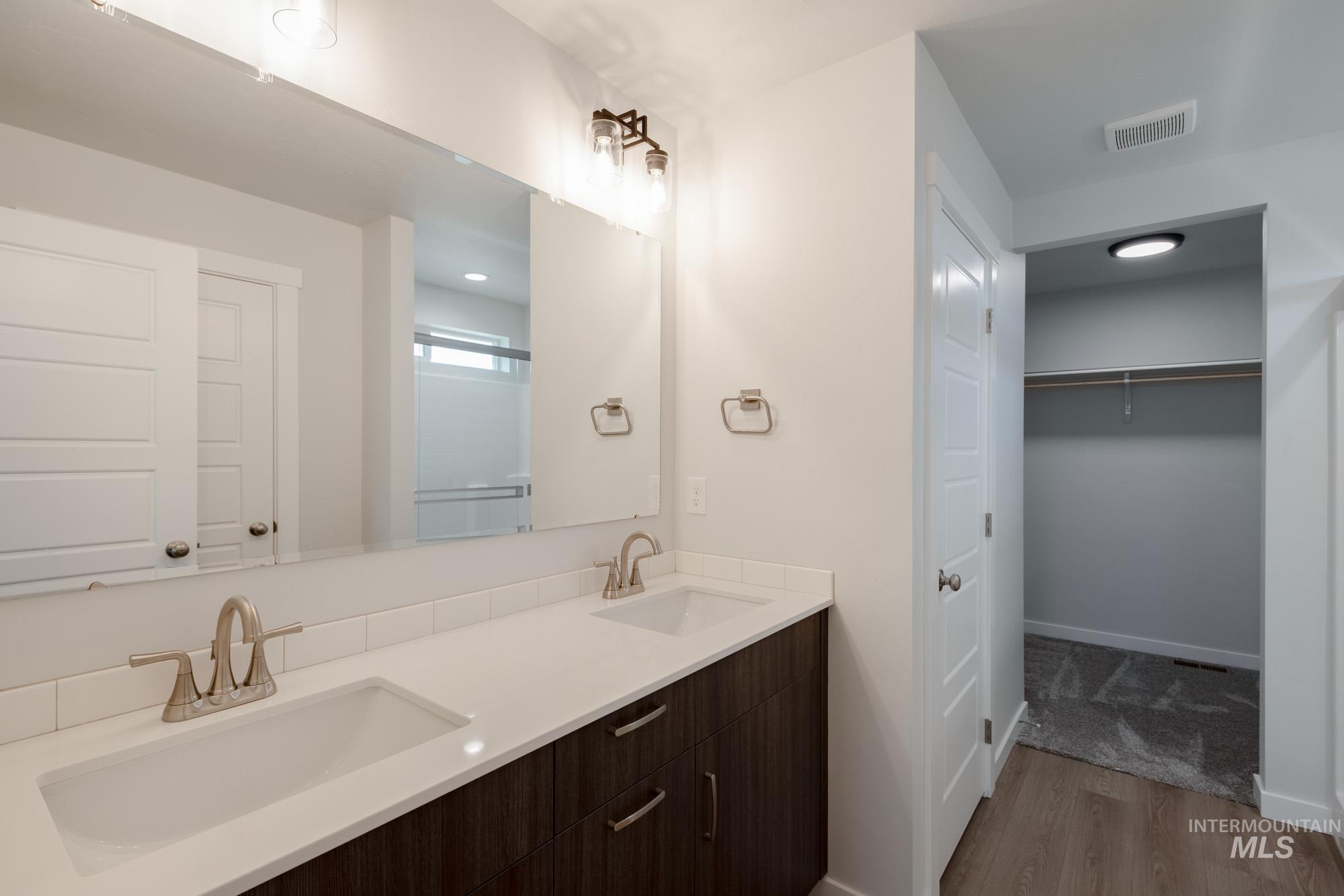 Full bathroom with a spacious closet, light wood-style floors, double vanity, and a shower with shower door