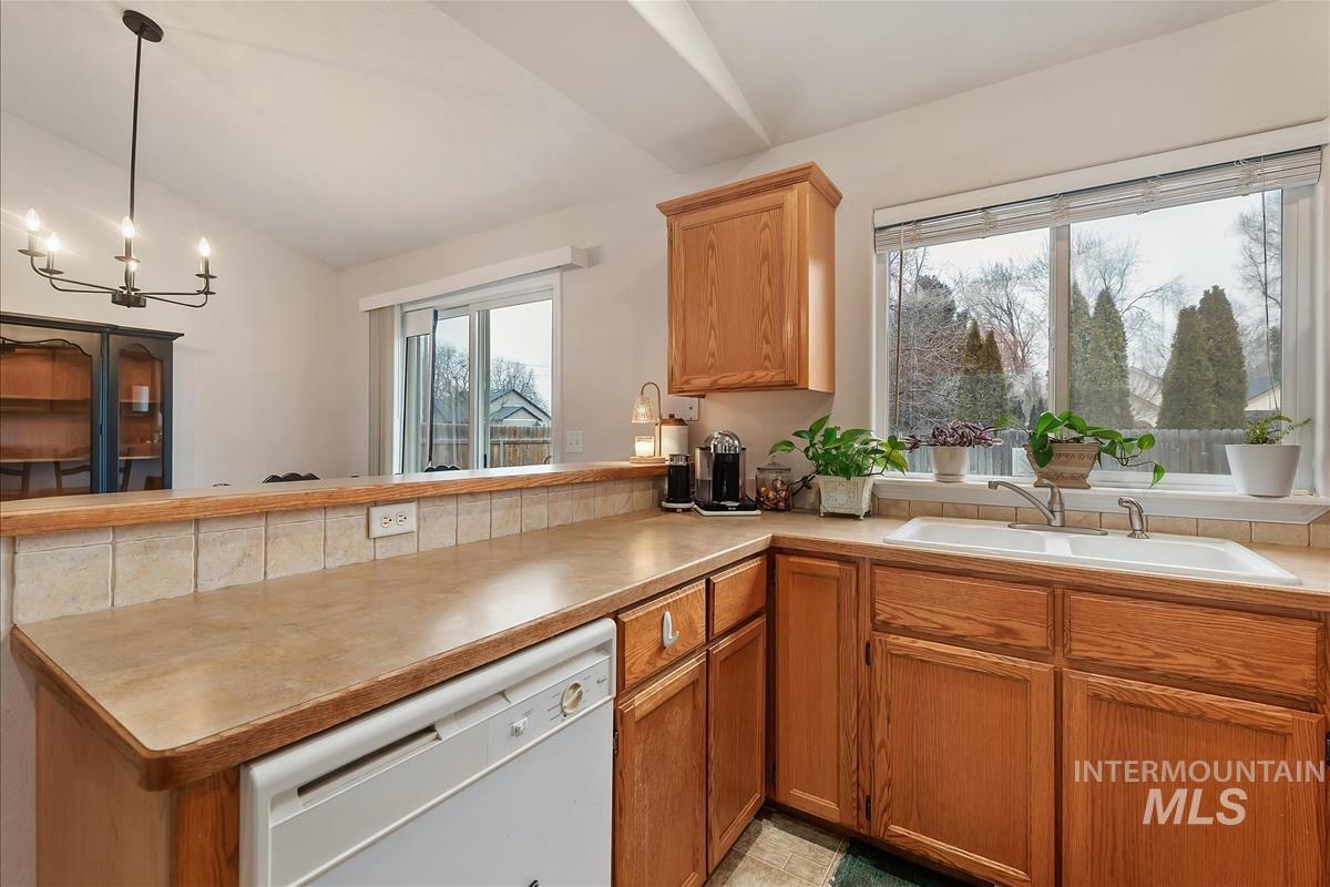 Kitchen with white dishwasher, light countertops, a peninsula, hanging light fixtures, and vaulted ceiling