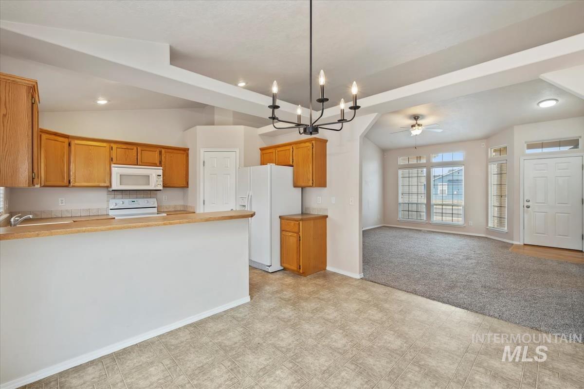 Kitchen featuring suspended lighting, white appliances, a peninsula, light colored carpet, and open floor plan