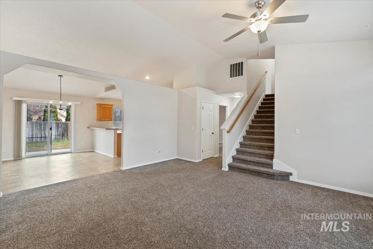 Unfurnished living room featuring carpet floors, a ceiling fan, vaulted ceiling, and suspended lighting