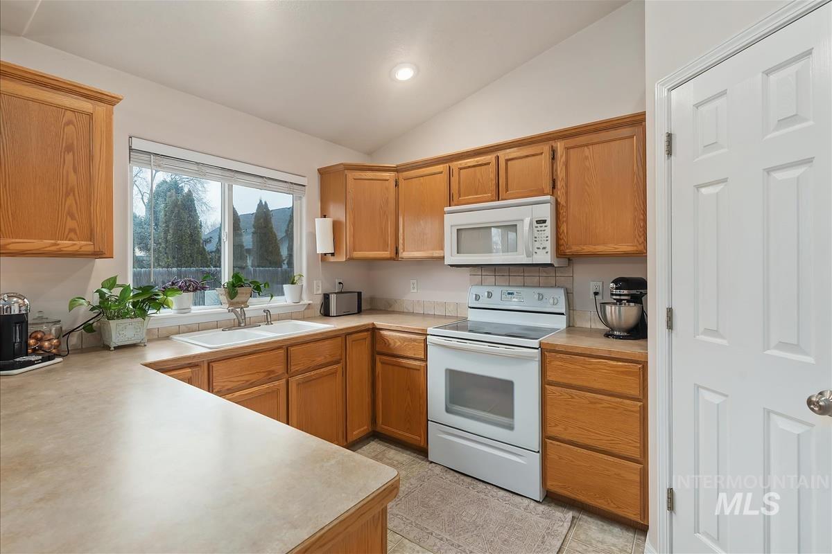 Kitchen with white appliances, light countertops, vaulted ceiling, recessed lighting, and brown cabinets