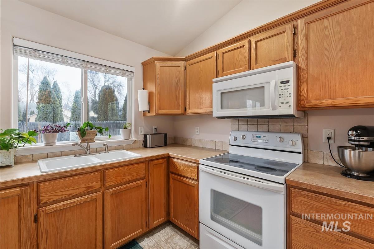 Kitchen with white appliances, light countertops, vaulted ceiling, and brown cabinetry