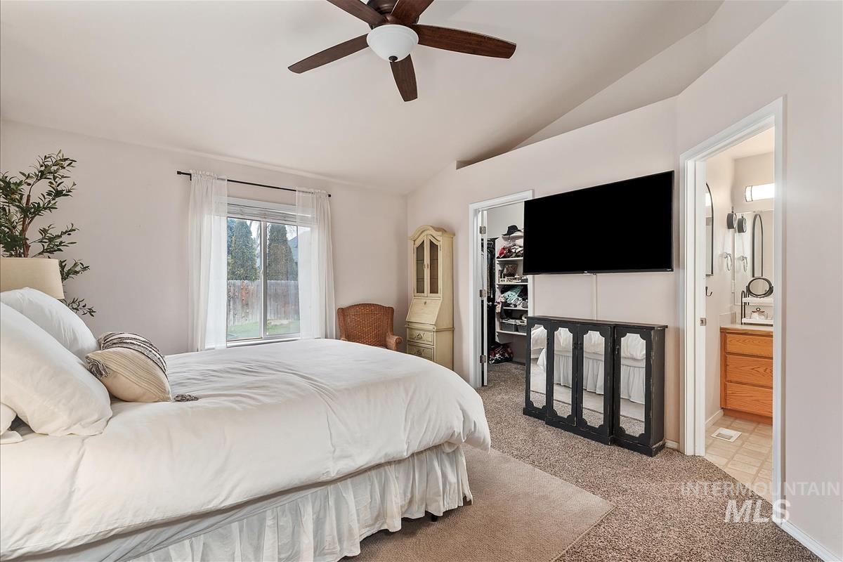 Bedroom featuring carpet flooring, a walk in closet, lofted ceiling, ensuite bath, and ceiling fan