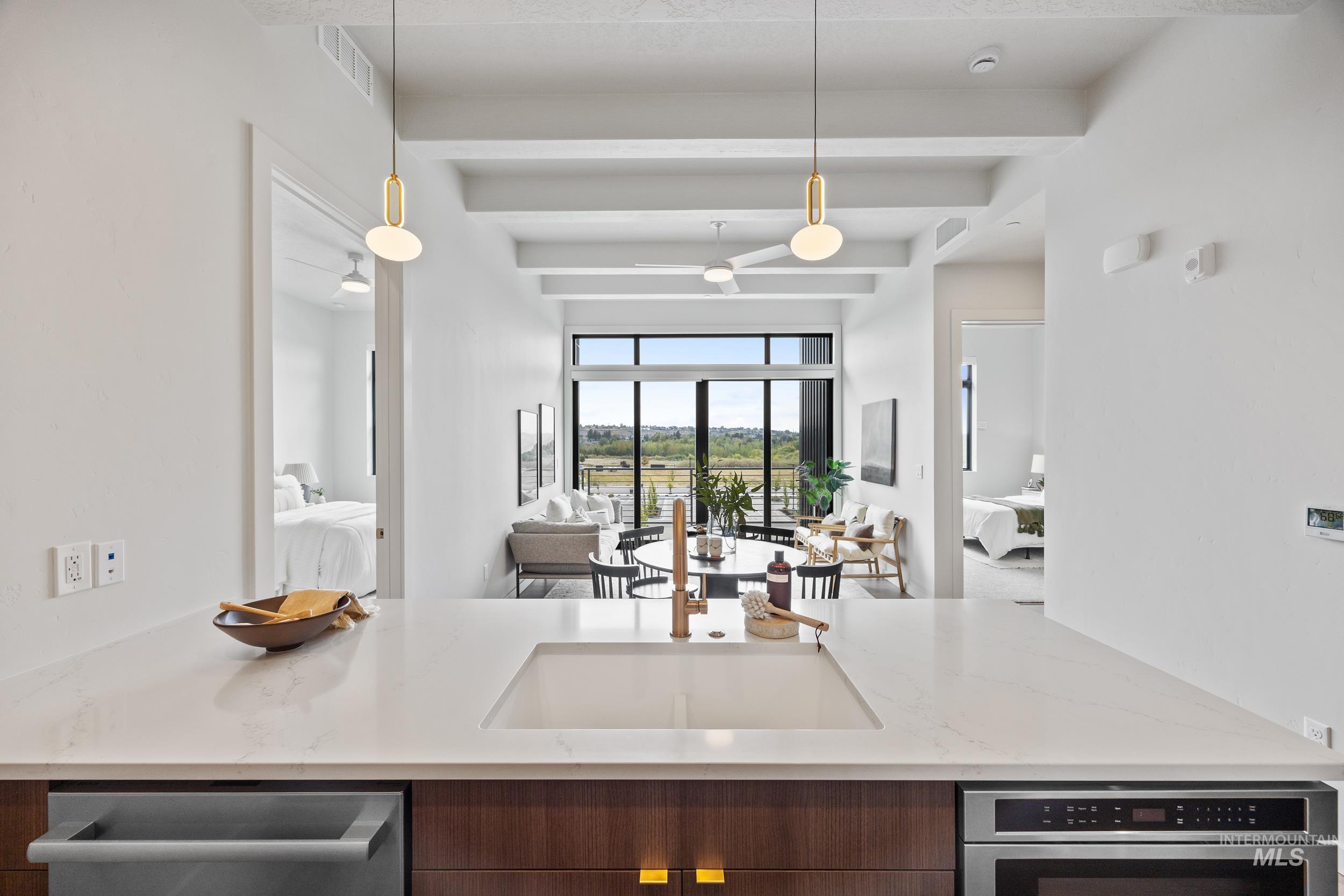 Kitchen featuring beam ceiling, light stone countertops, open floor plan, pendant lighting, and appliances with stainless steel finishes
