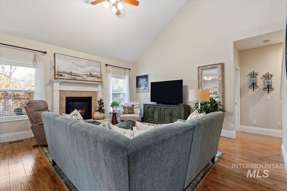 Living room with high vaulted ceiling, a tile fireplace, light wood-type flooring, and a ceiling fan