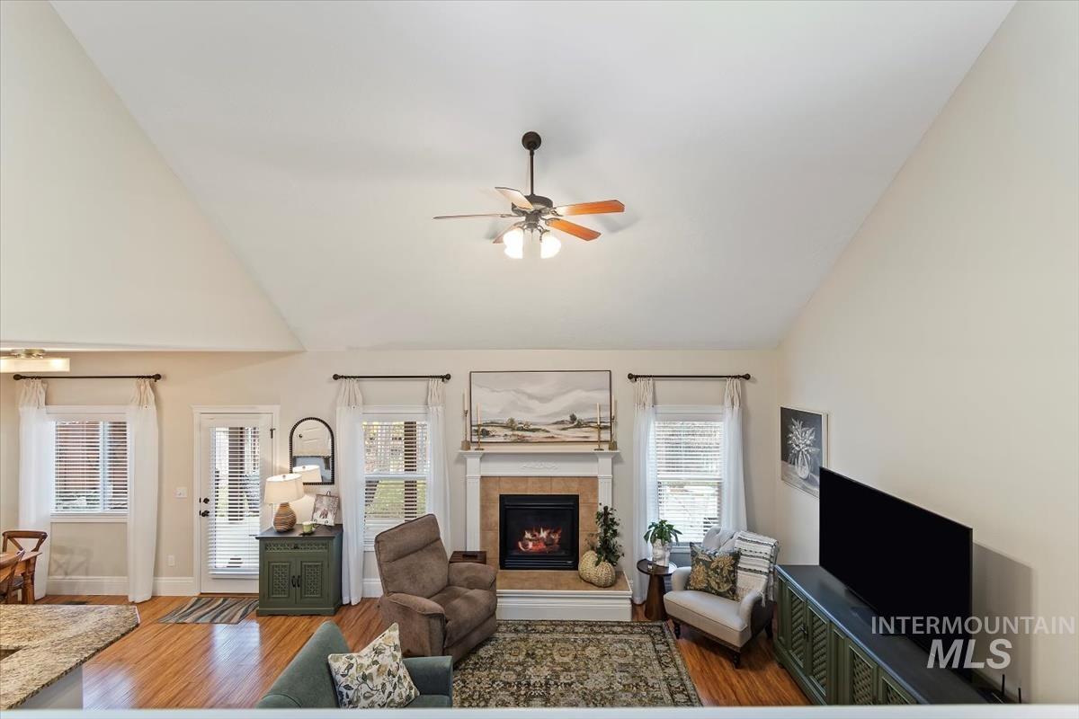 Living room with a tile fireplace, wood finished floors, lofted ceiling, and ceiling fan