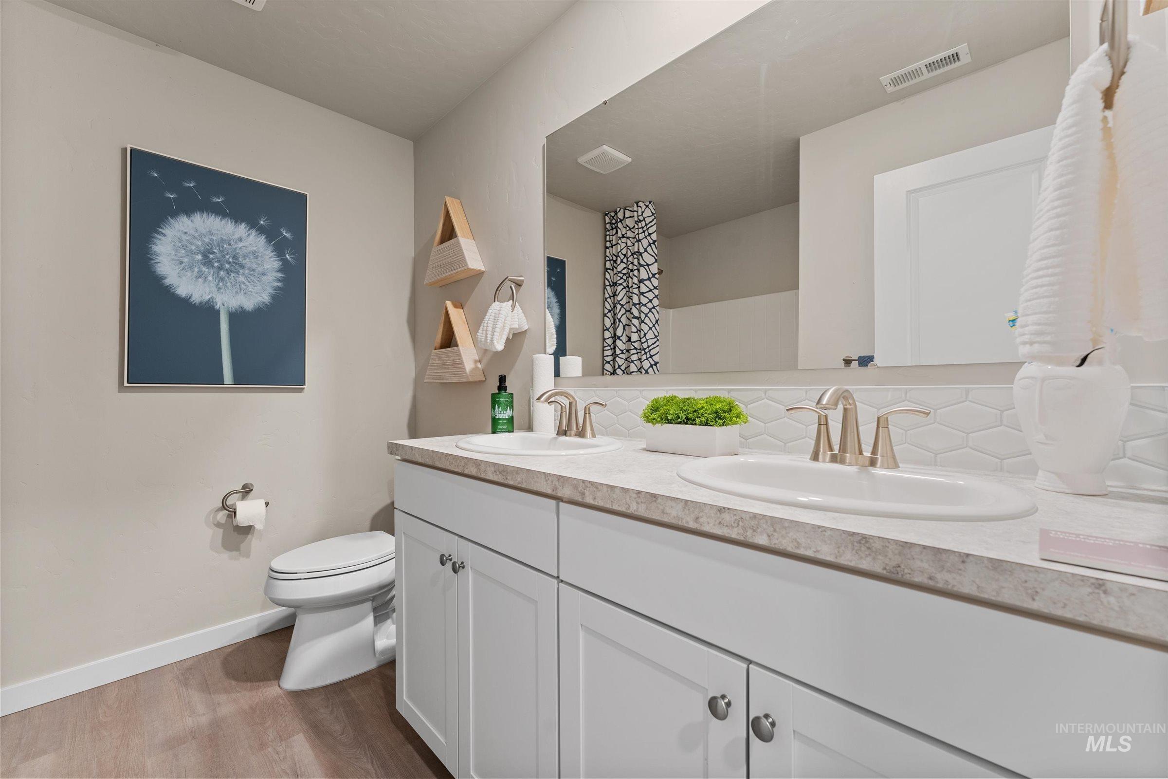 Bathroom featuring light wood-type flooring, double vanity, tasteful backsplash, and a shower with shower curtain
