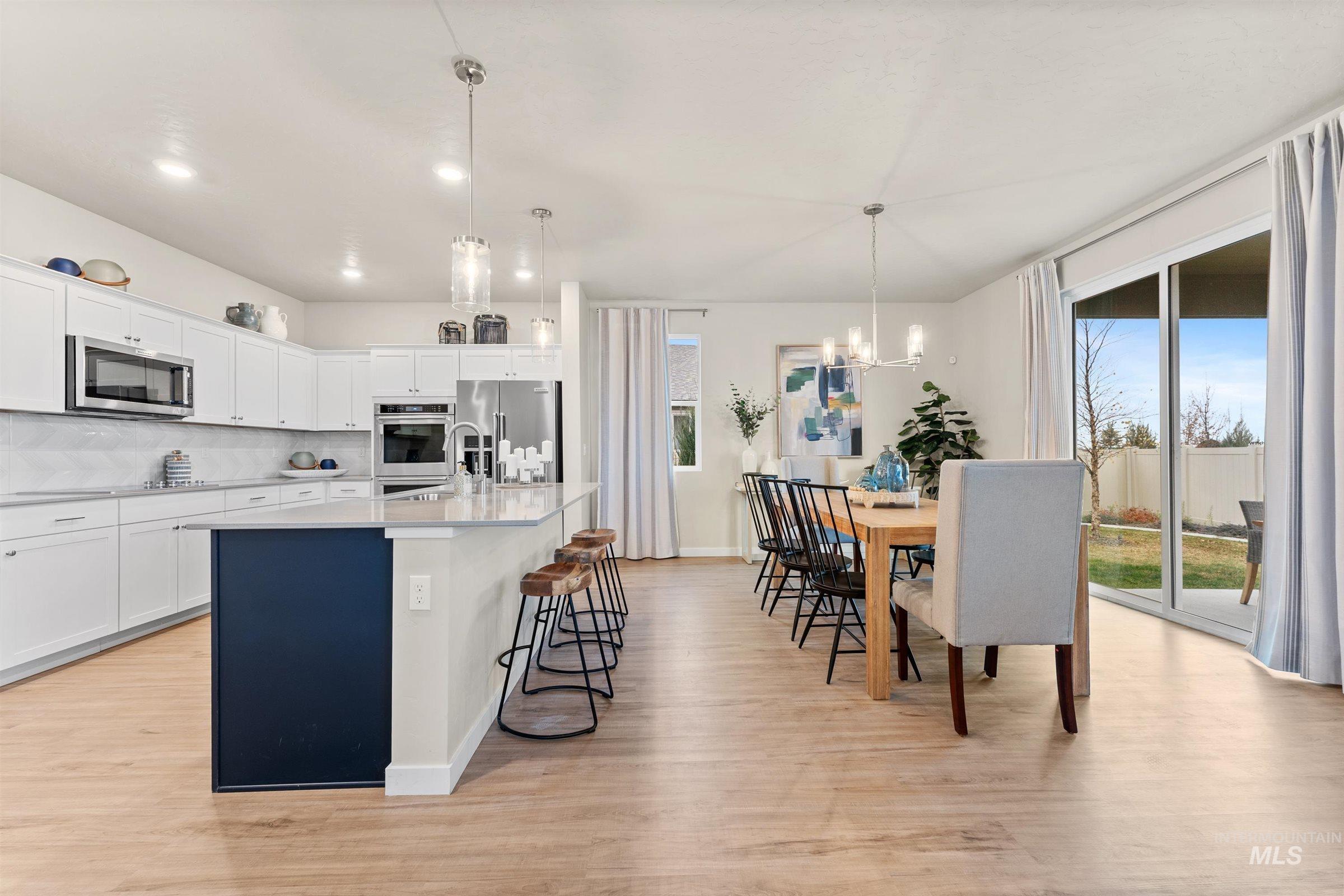 Kitchen featuring white cabinets, tasteful backsplash, a kitchen island with sink, decorative light fixtures, and appliances with stainless steel finishes