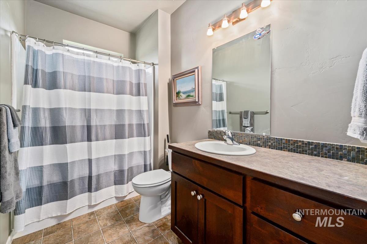 Full bath featuring vanity, dark tile patterned flooring, a shower with shower curtain, and backsplash