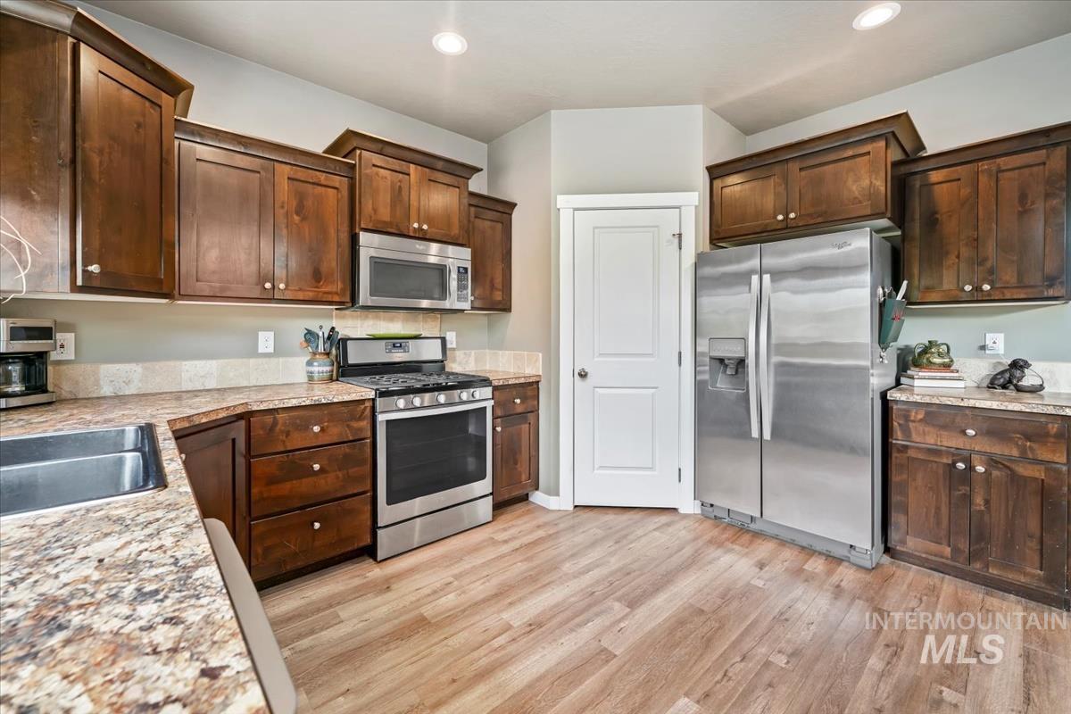 Kitchen with appliances with stainless steel finishes, light countertops, light wood-style floors, dark brown cabinets, and recessed lighting
