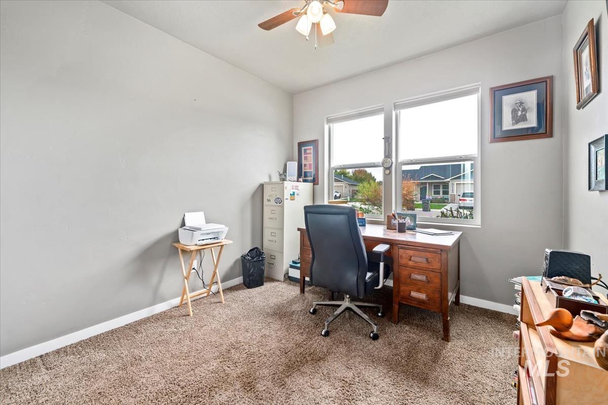 Carpeted home office featuring ceiling fan and baseboards