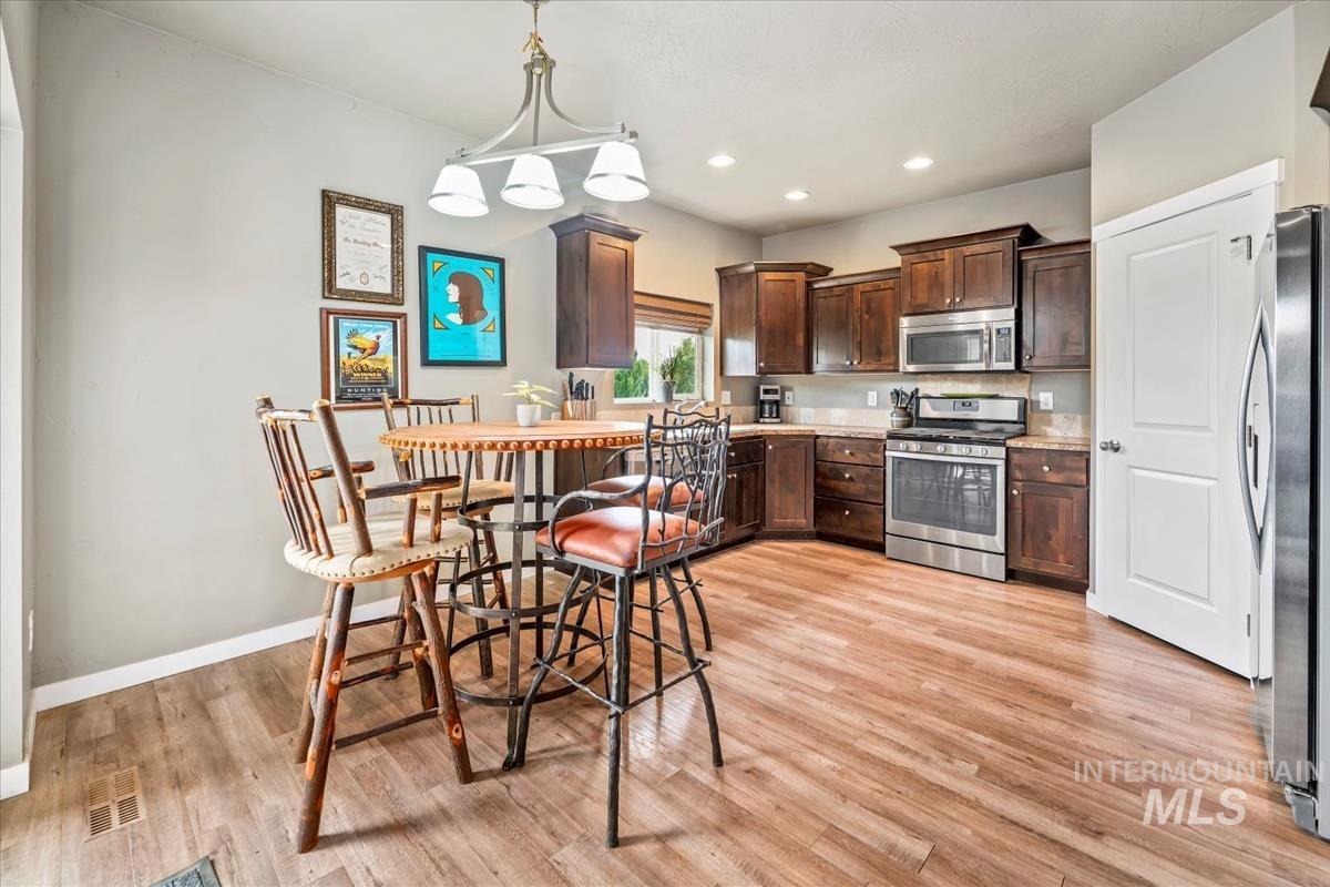 Kitchen with dark brown cabinetry, hanging light fixtures, appliances with stainless steel finishes, light wood-style floors, and recessed lighting