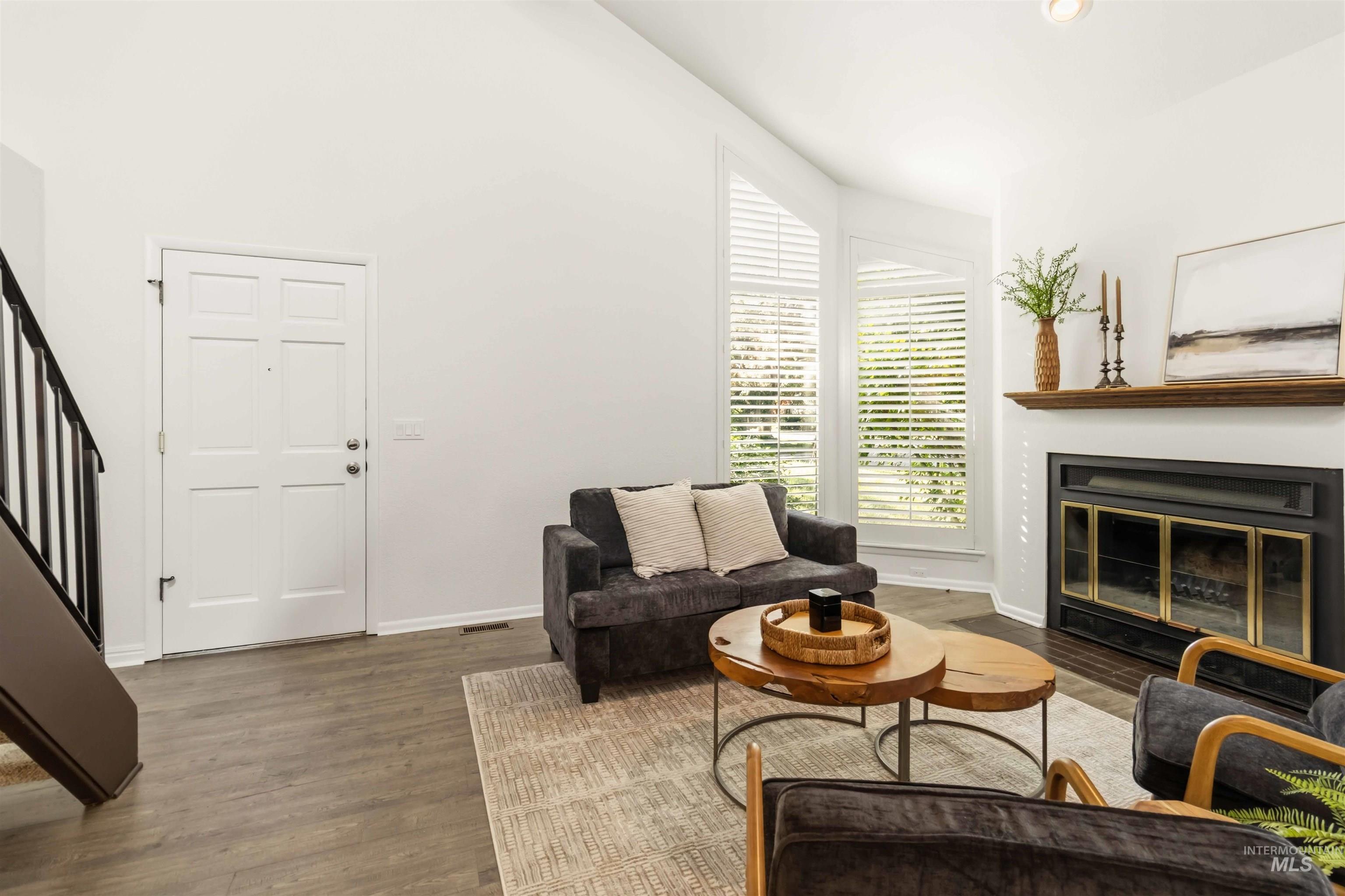 Living area featuring vaulted ceilings, wood-finish flooring, and a fireplace with a wood mantle
