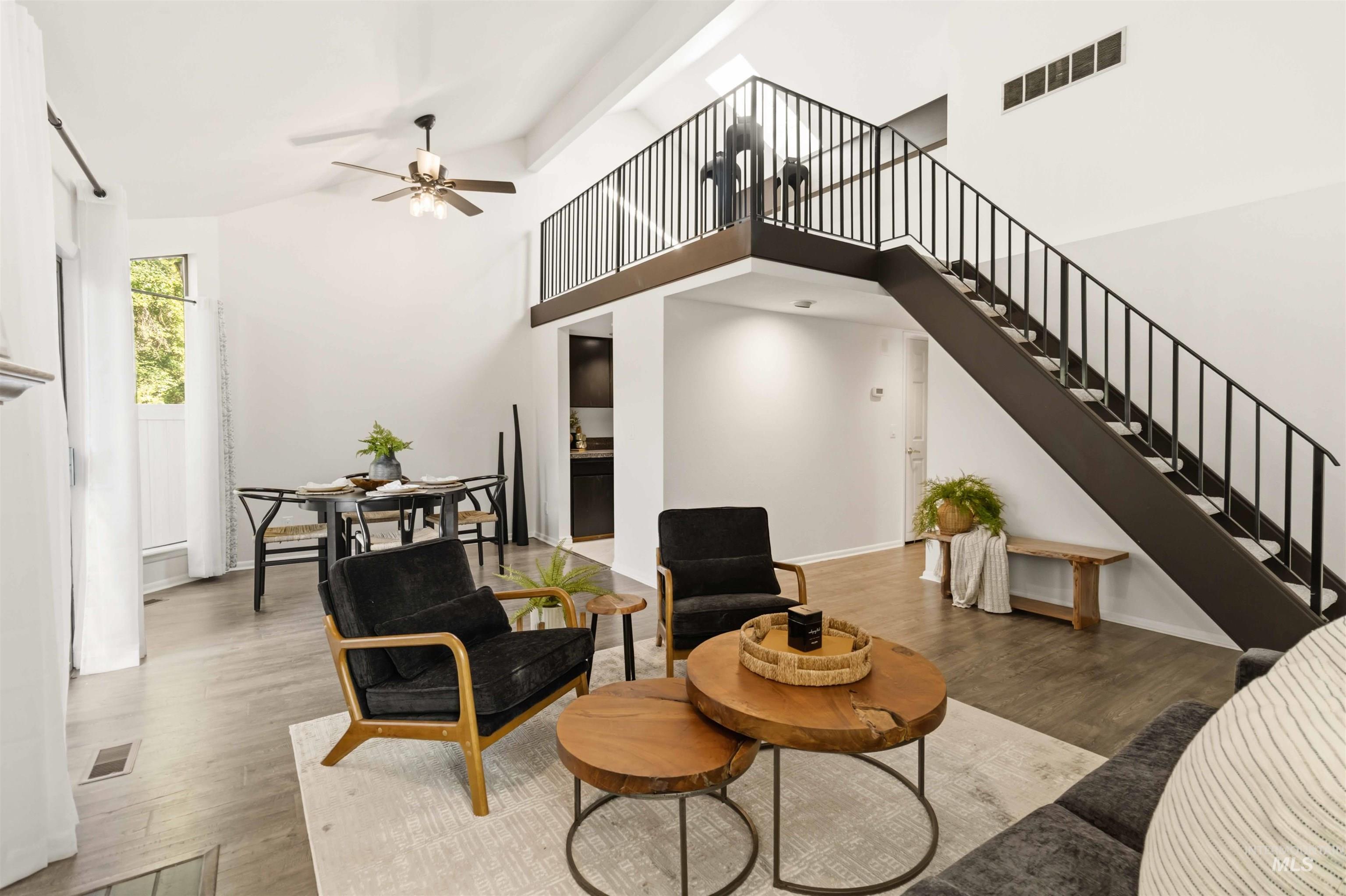 Voluminous living area featuring vaulted ceilings, wood-finish flooring, a contemporary staircase with black metal railing, and a ceiling fan