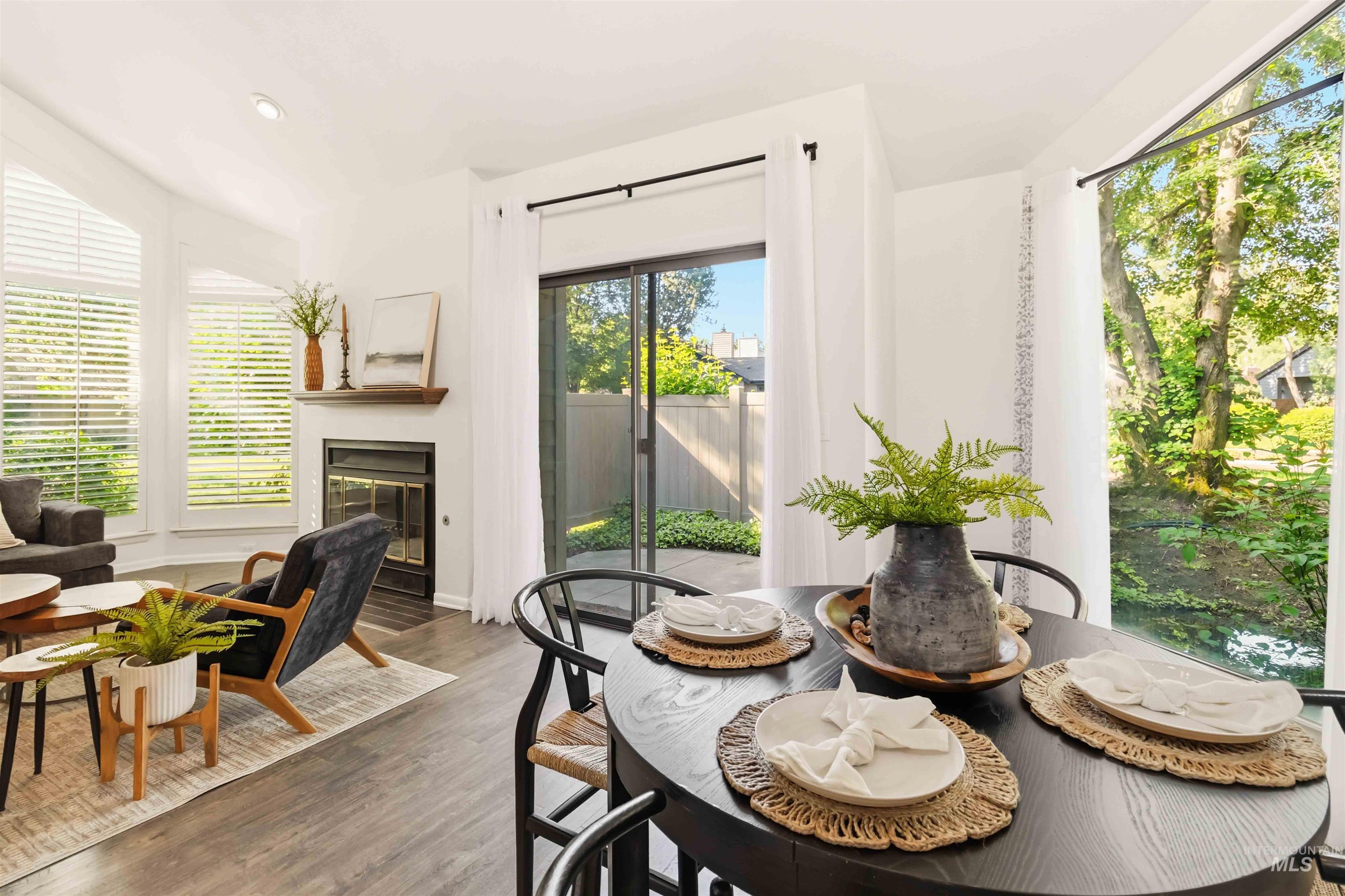 Open-concept living space featuring wood-finish flooring, a corner fireplace with a wood mantle, and bright windows with horizontal blinds