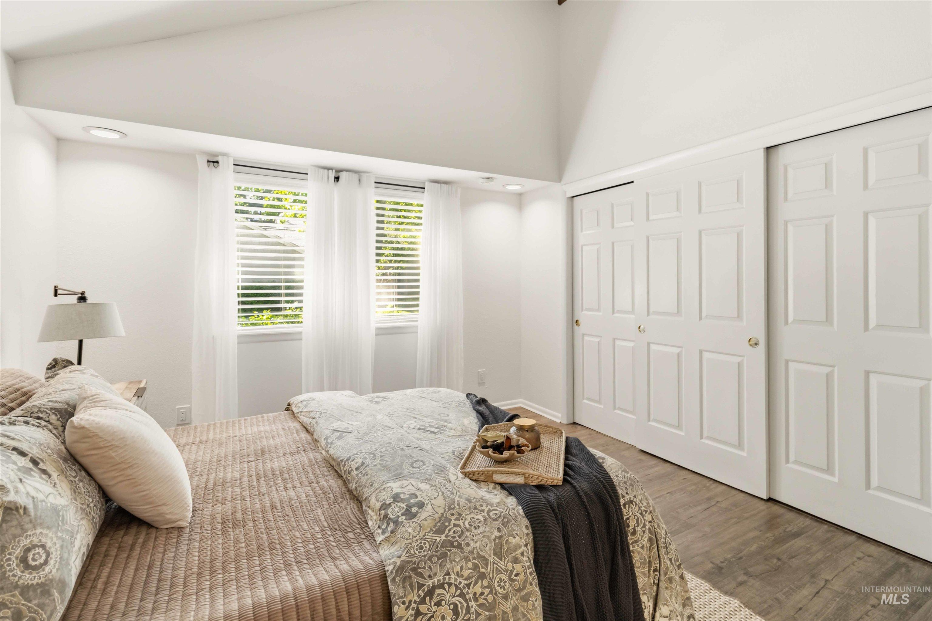 Vaulted ceiling bedroom featuring two windows with horizontal blinds, wood-finish flooring, two large sliding closet doors, and recessed lighting