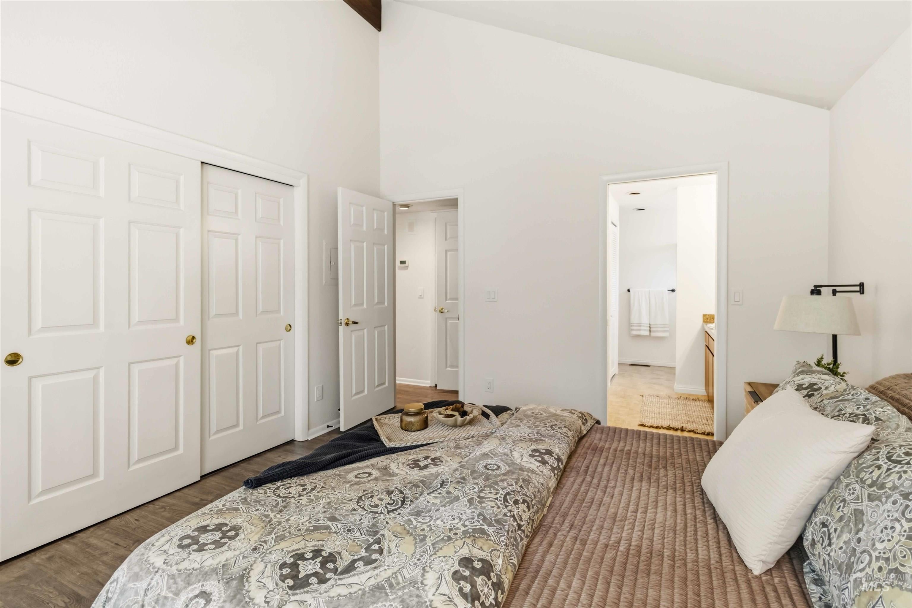 Vaulted ceiling room featuring wood-finish flooring, white paneled closet doors, and an open doorway to a bathroom with a vanity