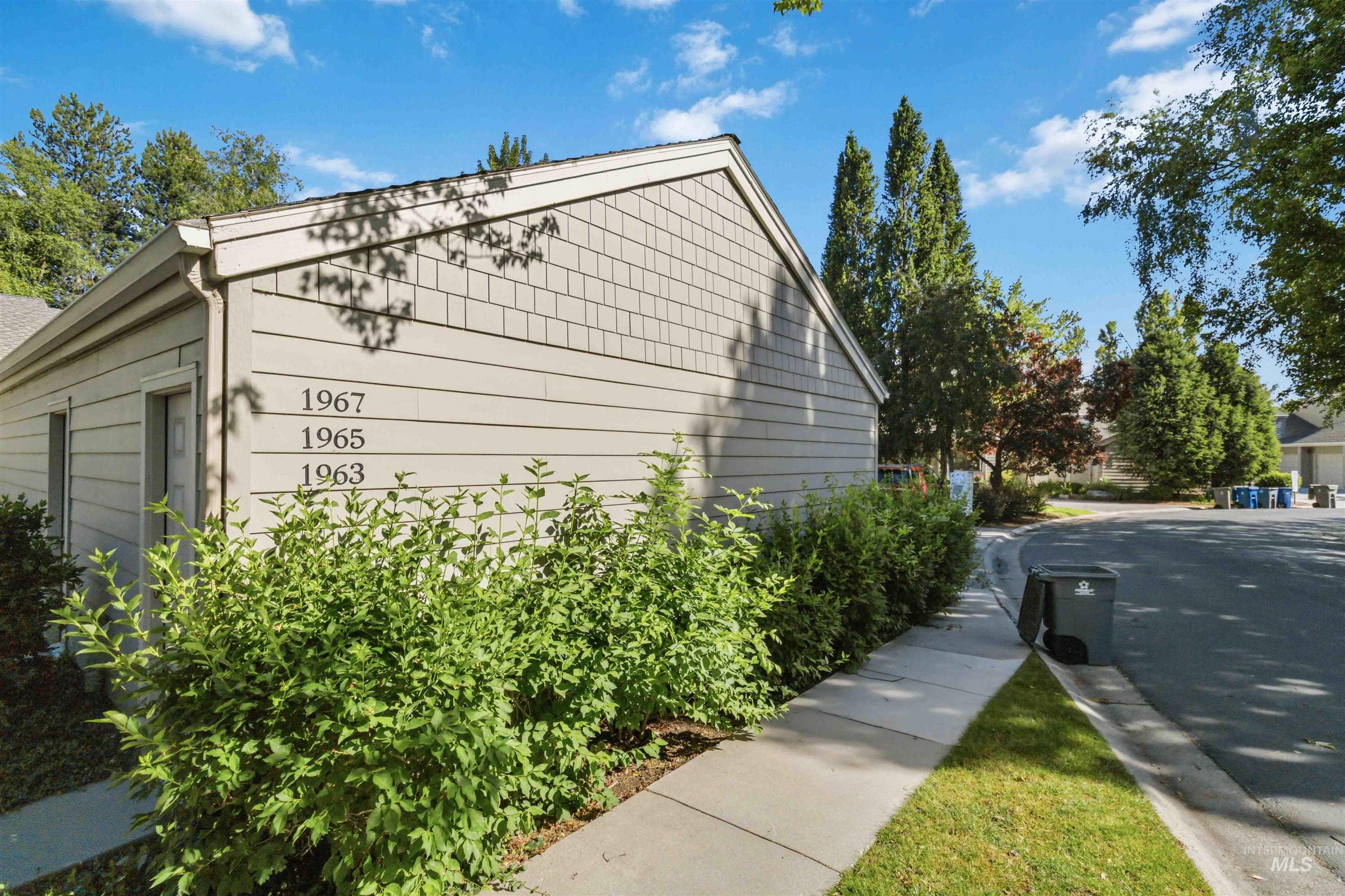 Exterior featuring horizontal siding with shingle accents, concrete walkway, established shrubbery, and mature trees