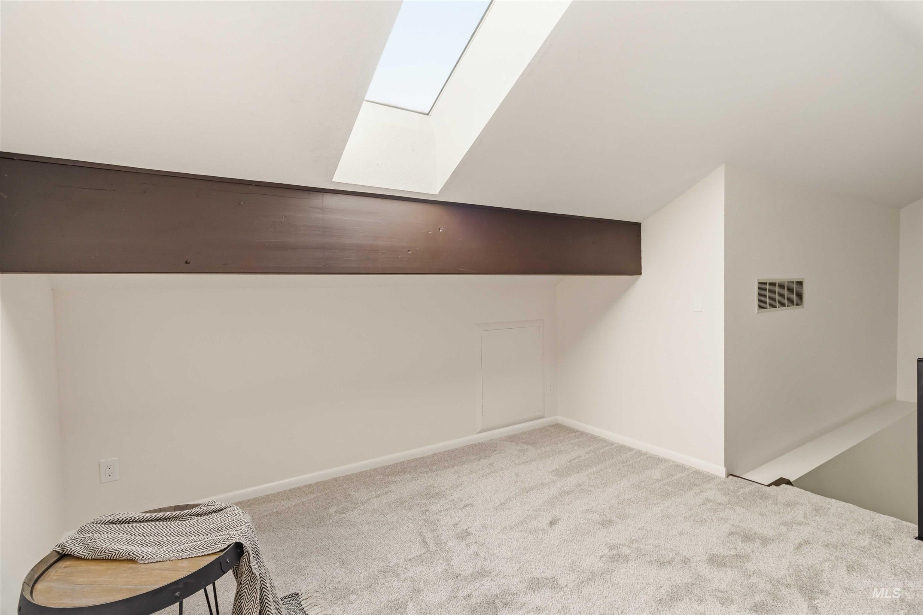 Loft space featuring a prominent skylight, light-colored carpeting, fresh painted walls, a dark ceiling beam