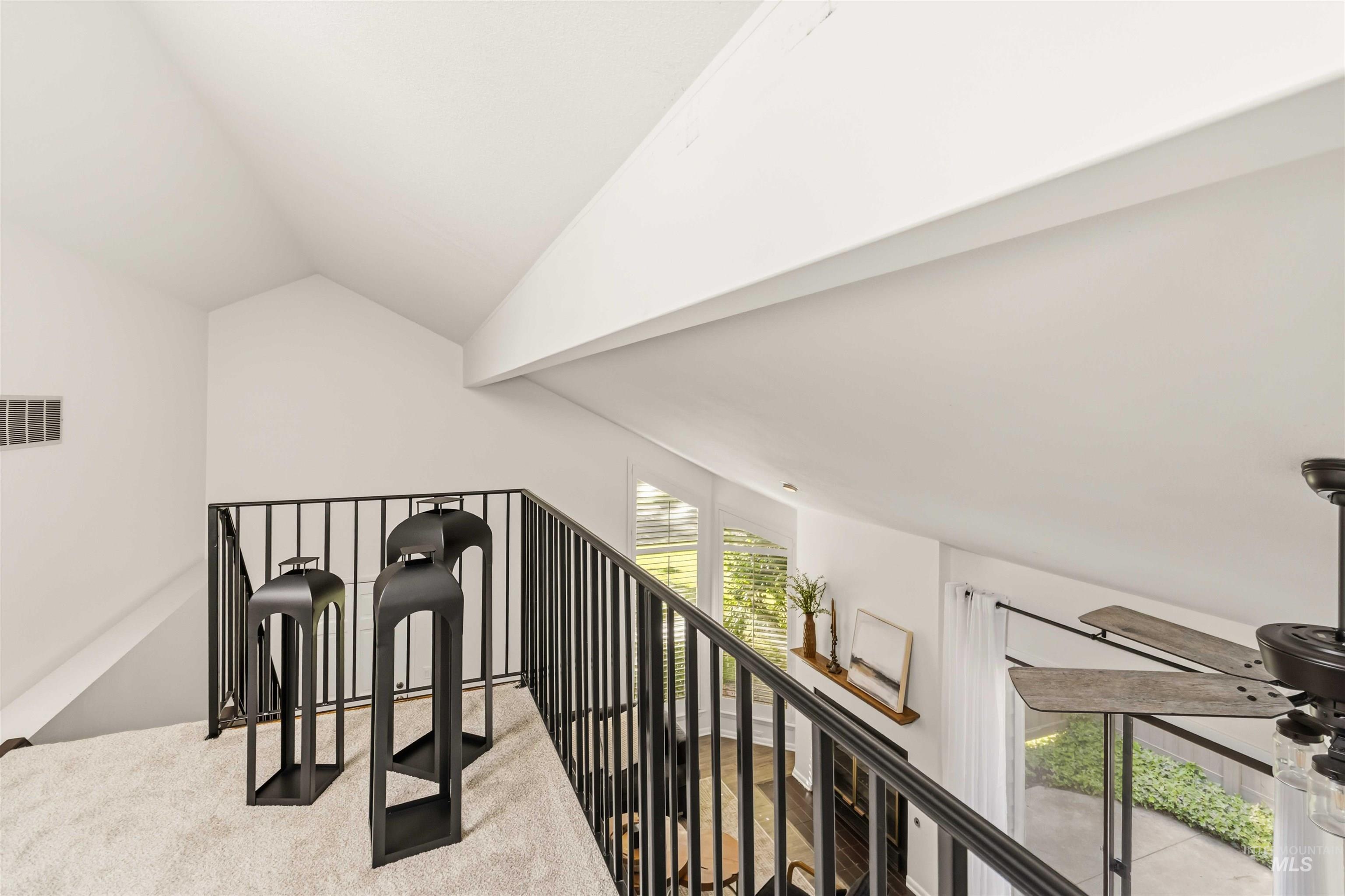 Carpeted loft area featuring a black metal railing, vaulted white ceilings, and natural light from a skylight