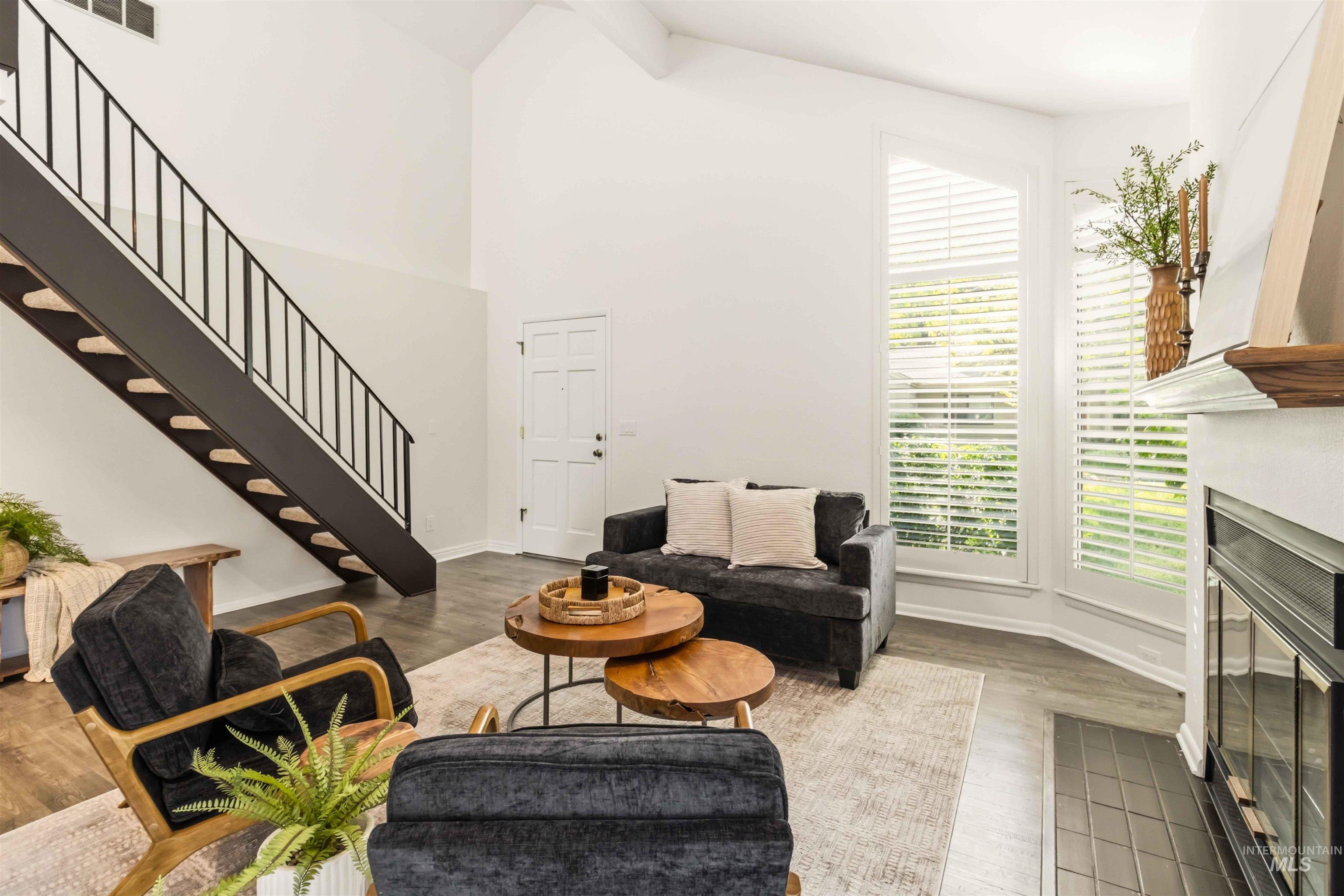 Vaulted living space featuring a modern staircase with black metal railings, a fireplace with a tiled hearth, and large windows with plantation shutters