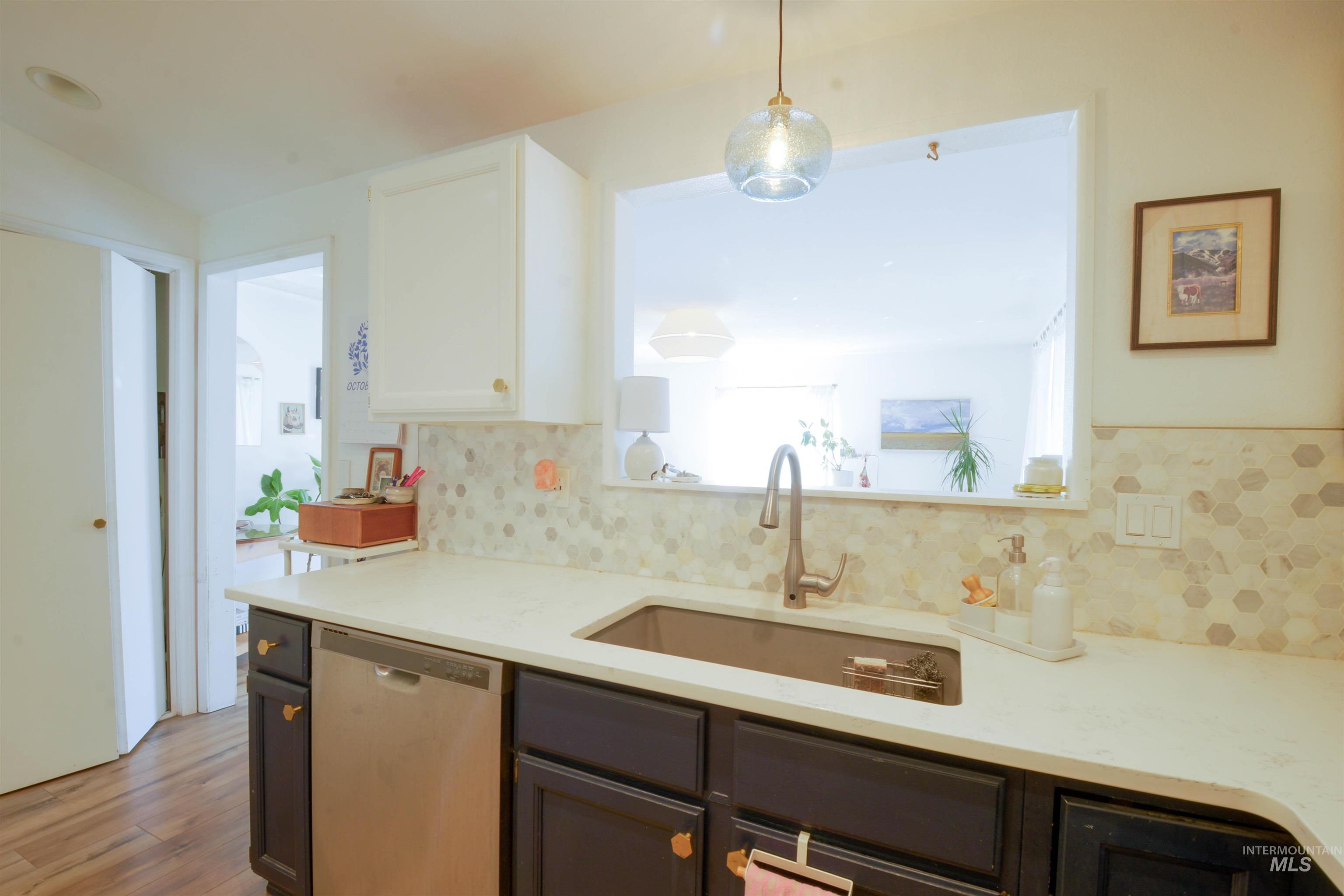Kitchen with white cabinetry, stainless steel dishwasher, decorative light fixtures, light wood-style flooring, and light stone countertops