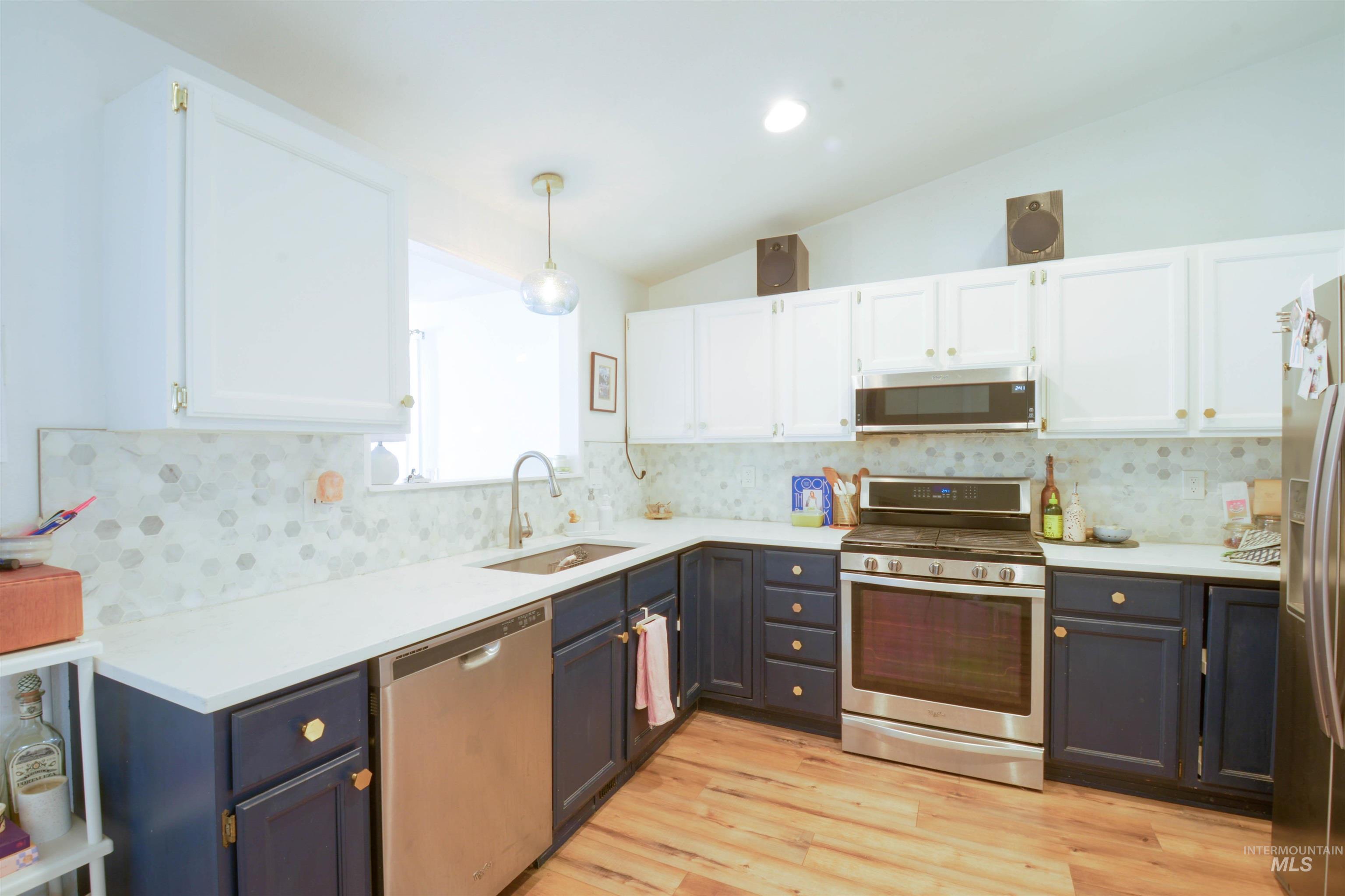 Kitchen with white cabinets, stainless steel appliances, vaulted ceiling, pendant lighting, and light wood finished floors