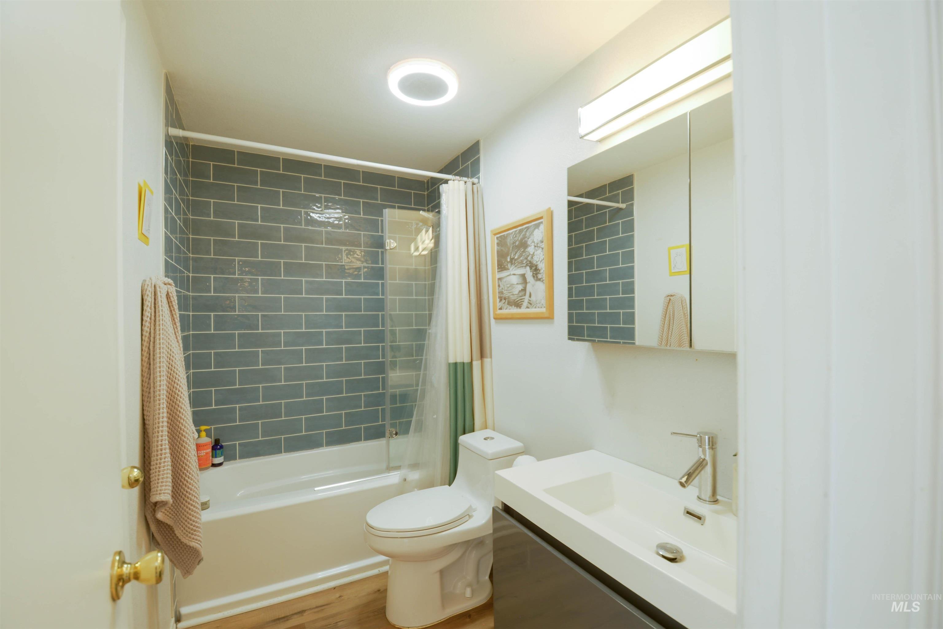 Bathroom featuring shower / bathtub combination with curtain, vanity, and light wood finished floors