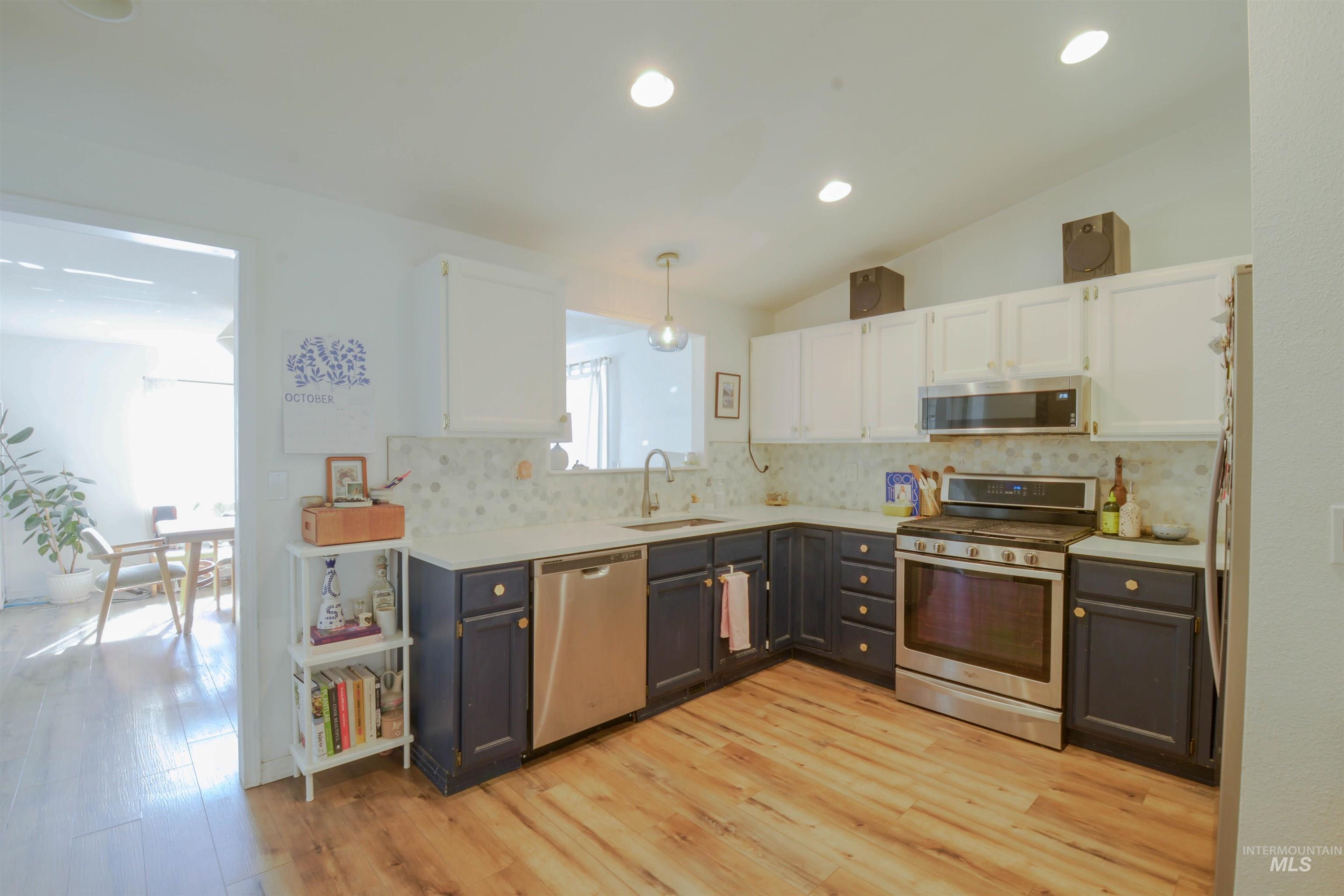 Kitchen with white cabinetry, appliances with stainless steel finishes, lofted ceiling, pendant lighting, and light wood-style flooring