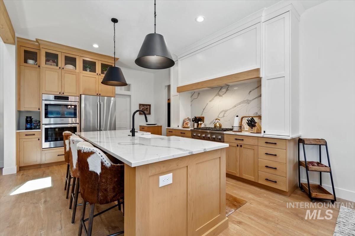 Kitchen featuring light brown cabinets, light stone counters, light wood finished floors, appliances with stainless steel finishes, and recessed lighting