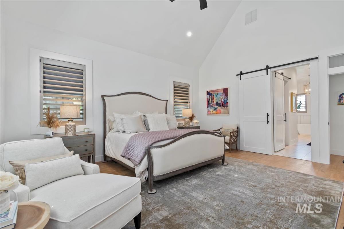 Bedroom with high vaulted ceiling, a barn door, a ceiling fan, wood finished floors, and recessed lighting