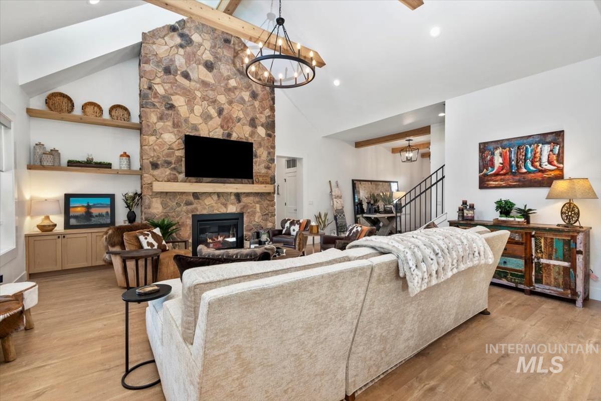 Living room with a fireplace, beam ceiling, light wood-type flooring, a chandelier, and high vaulted ceiling