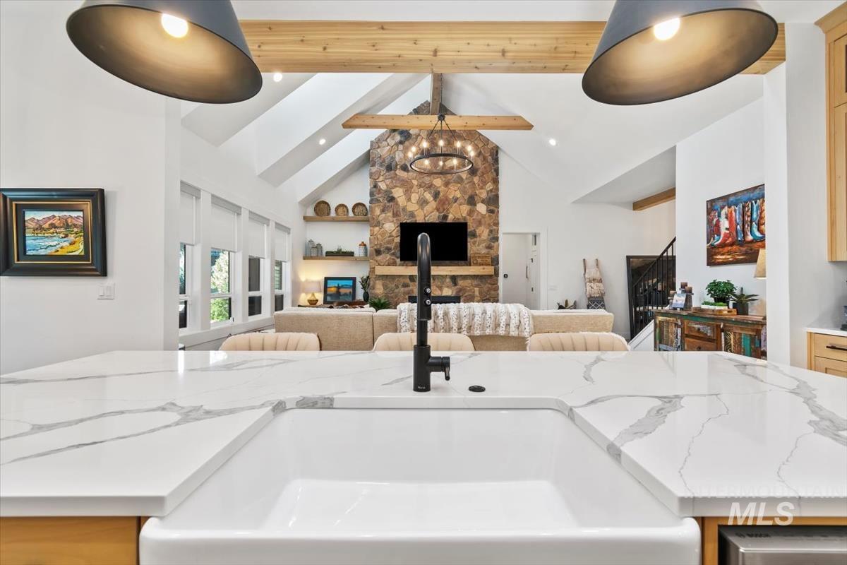 Kitchen with beam ceiling, light stone countertops, high vaulted ceiling, open floor plan, and a kitchen island with sink