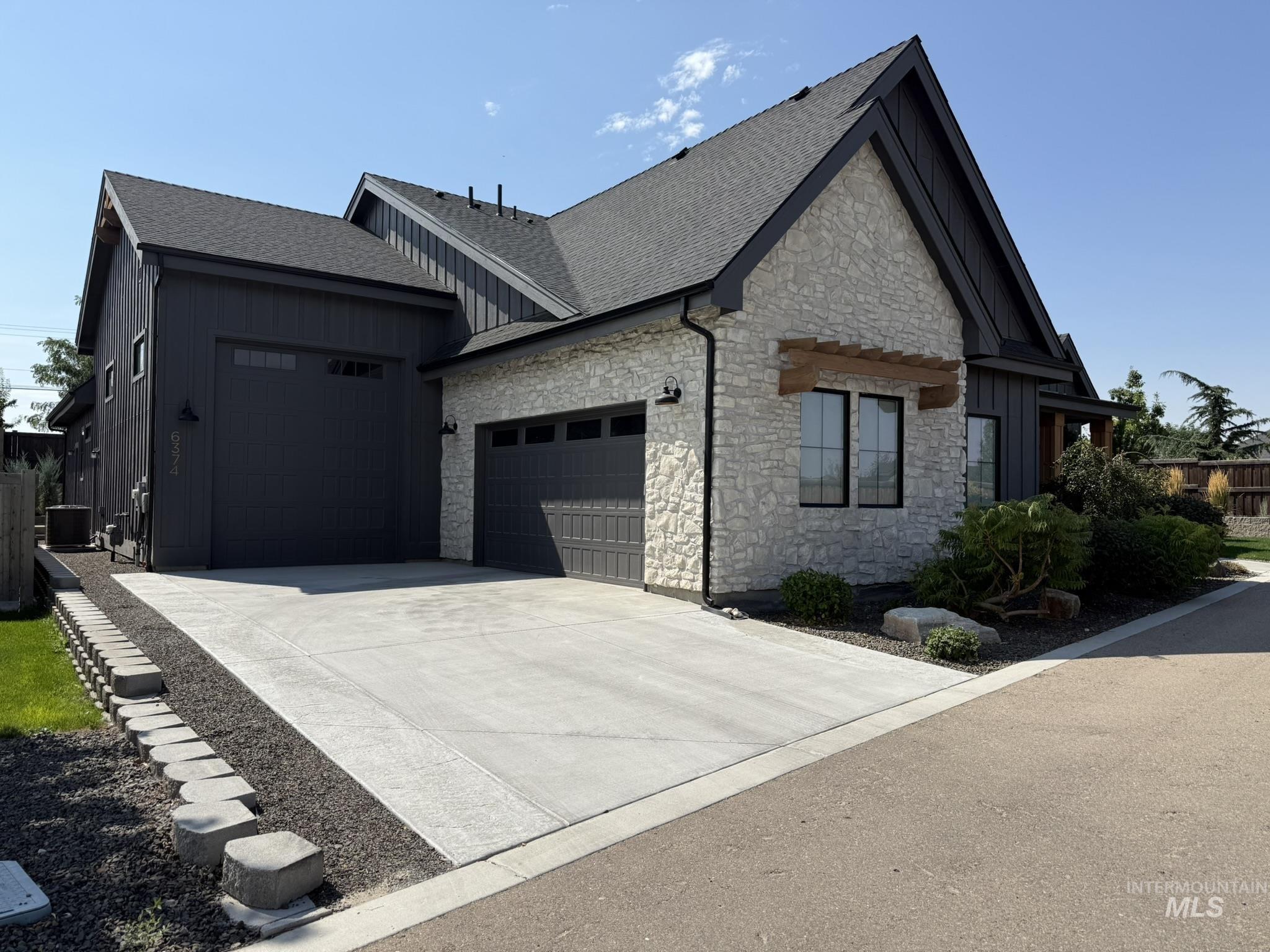 View of side of home with board and batten siding, stone siding, a shingled roof, and an attached garage